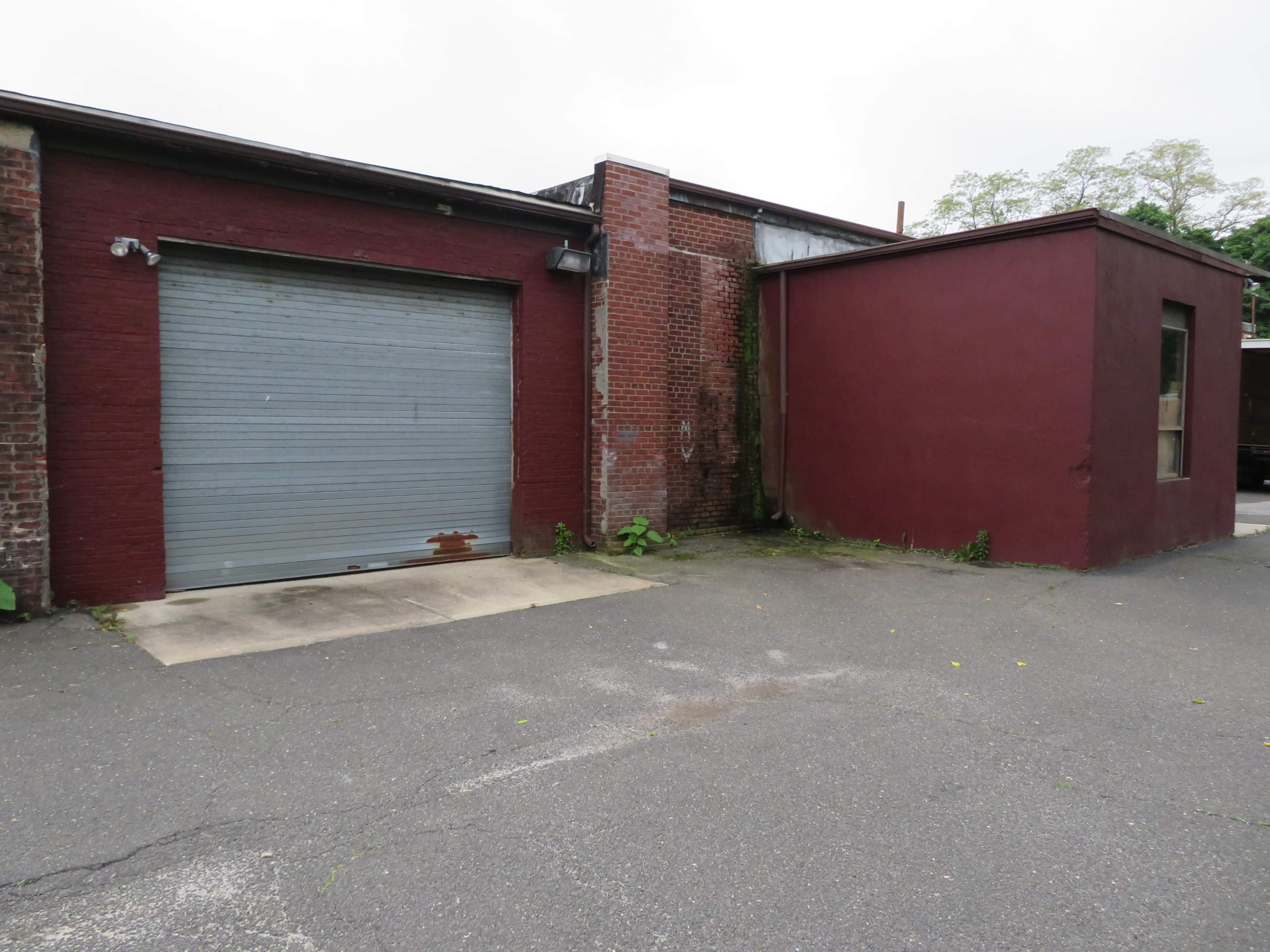 The image shows a brick building with a gray garage door and a maroon structure adjacent to it, set on a paved surface.