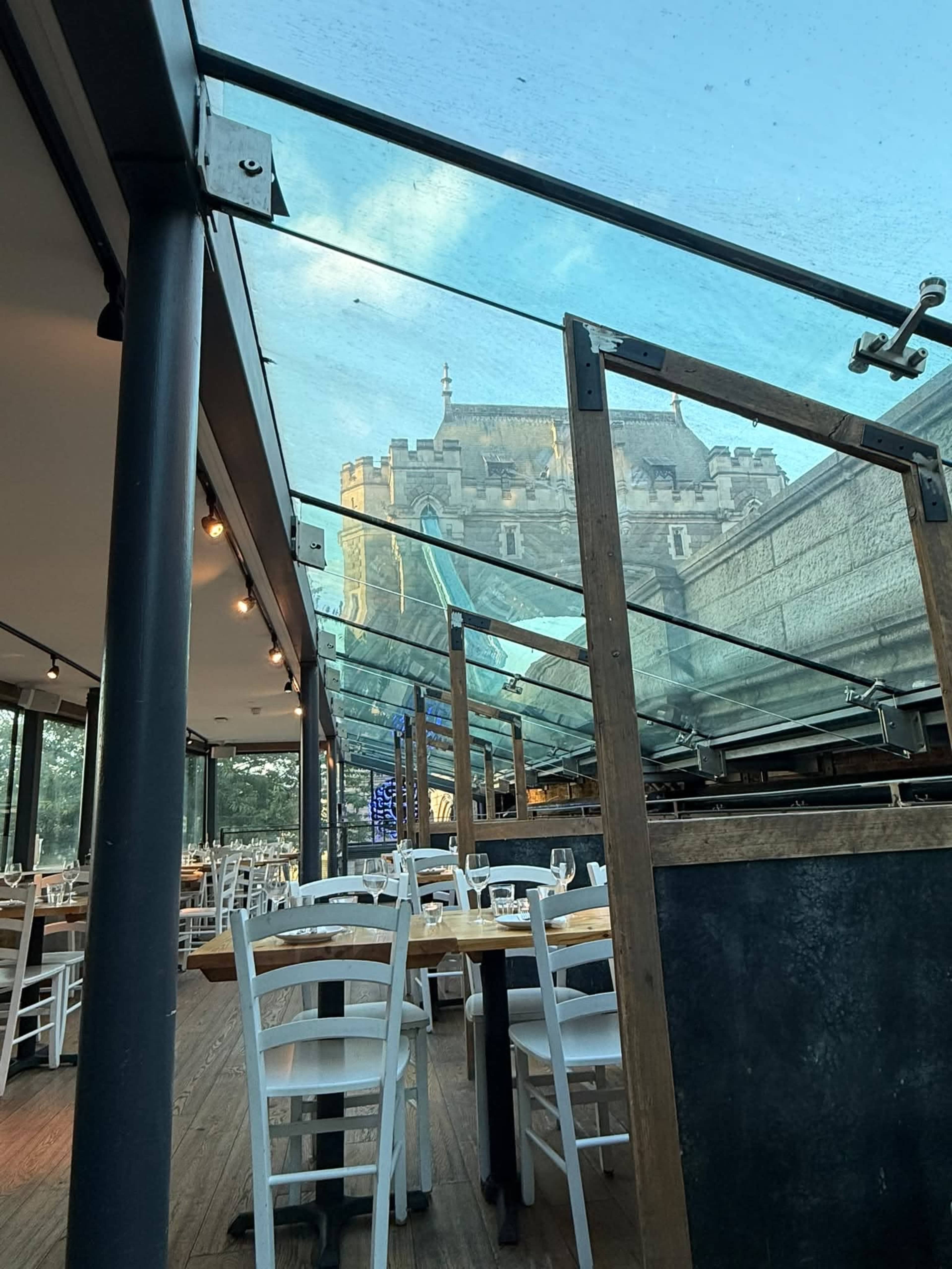 The image shows an empty restaurant with white tables and chairs, featuring a transparent roof that allows a view of a castle in the background.
