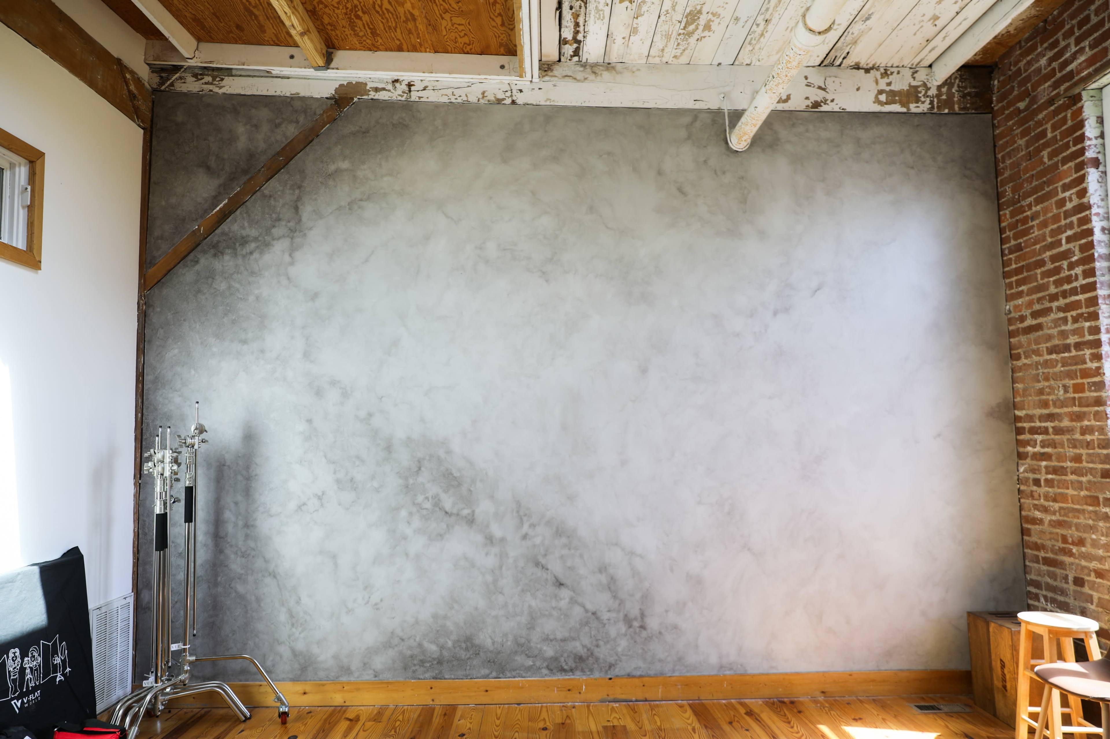 A spacious room with a textured gray wall, wooden floorboards, and exposed brick accents.