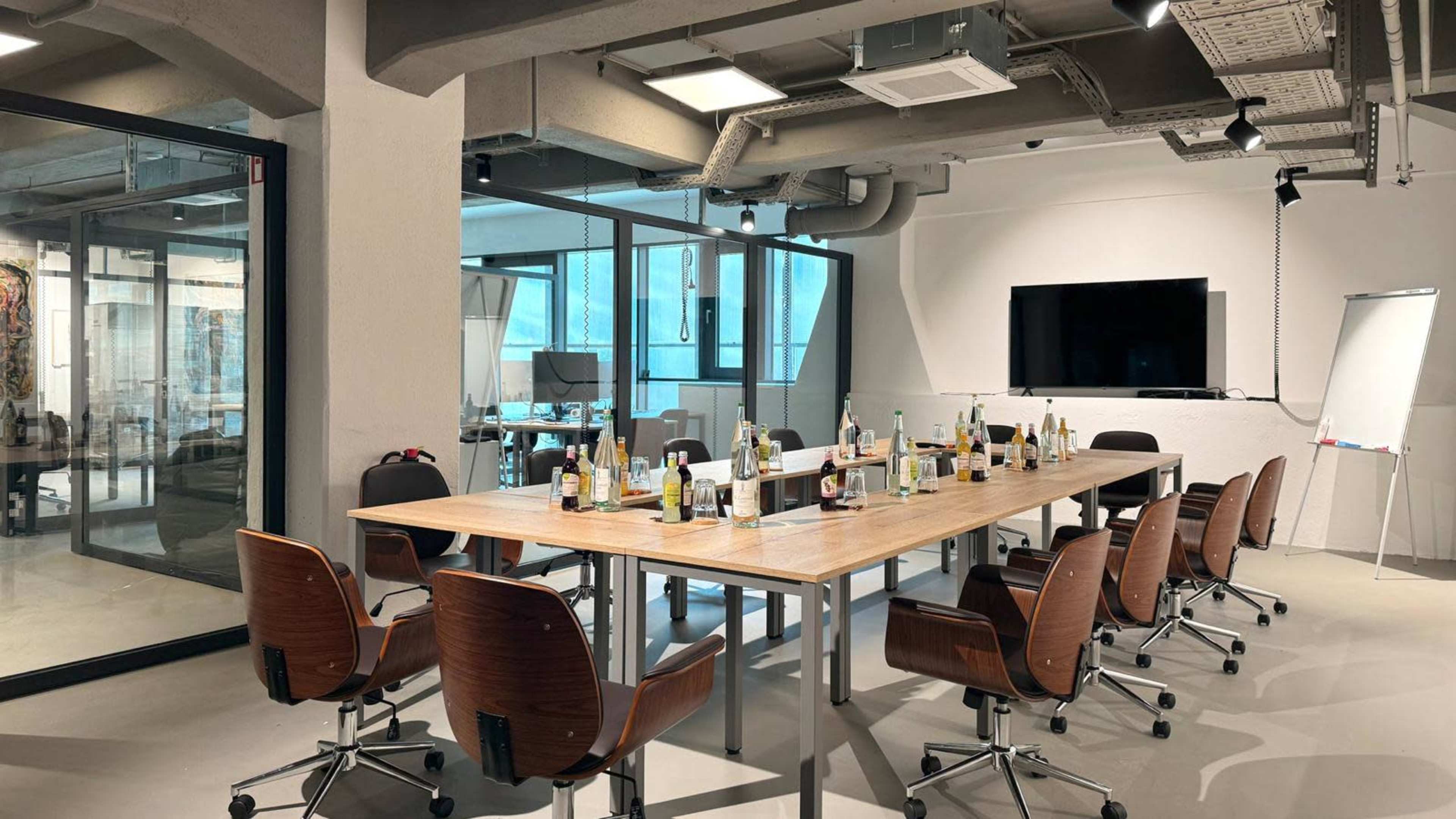 A conference room with a large table surrounded by chairs, featuring empty bottles and a presentation screen on the wall.