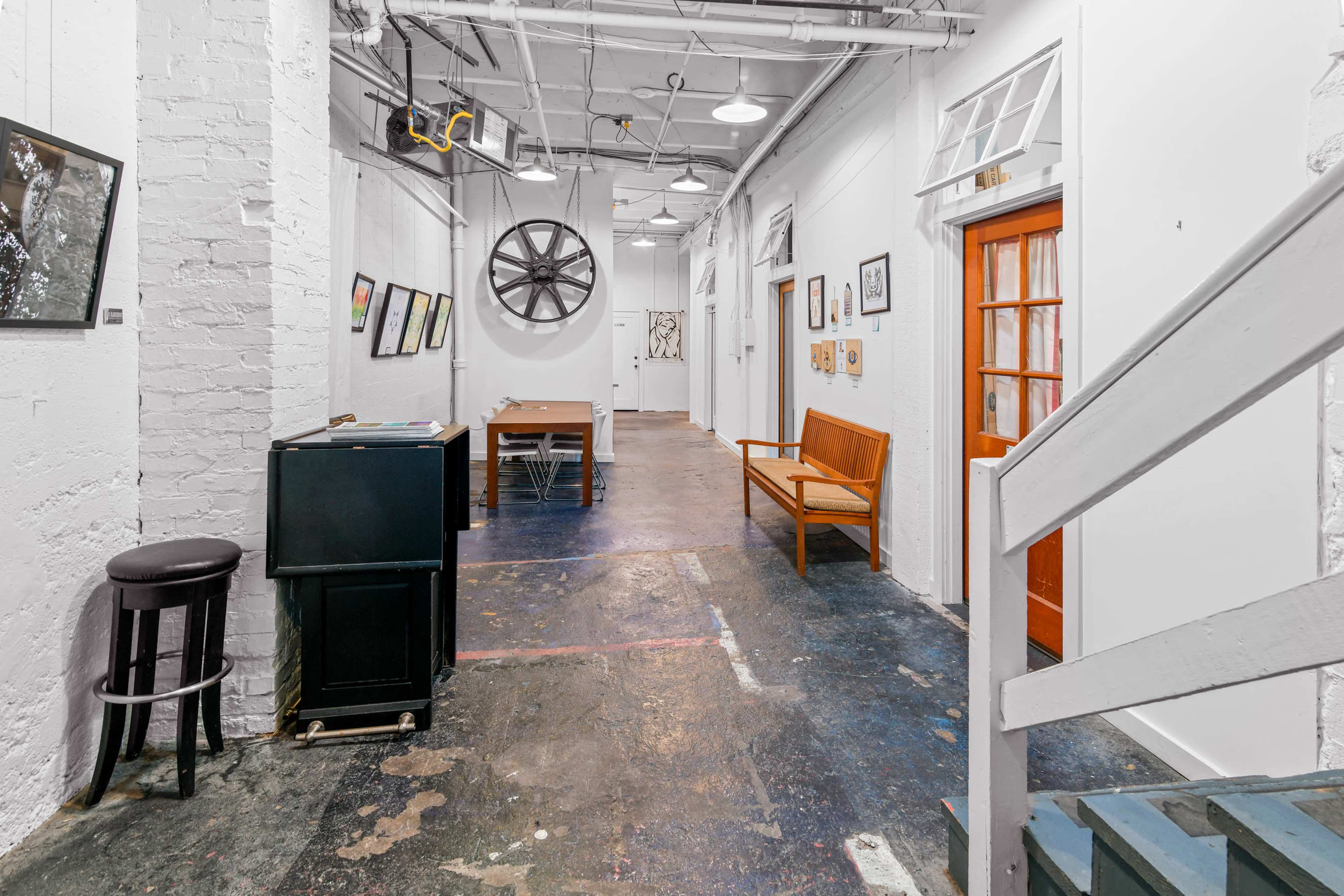 A stark, open hallway with white walls, a wooden bench, a table, and various artworks displayed along the walls.