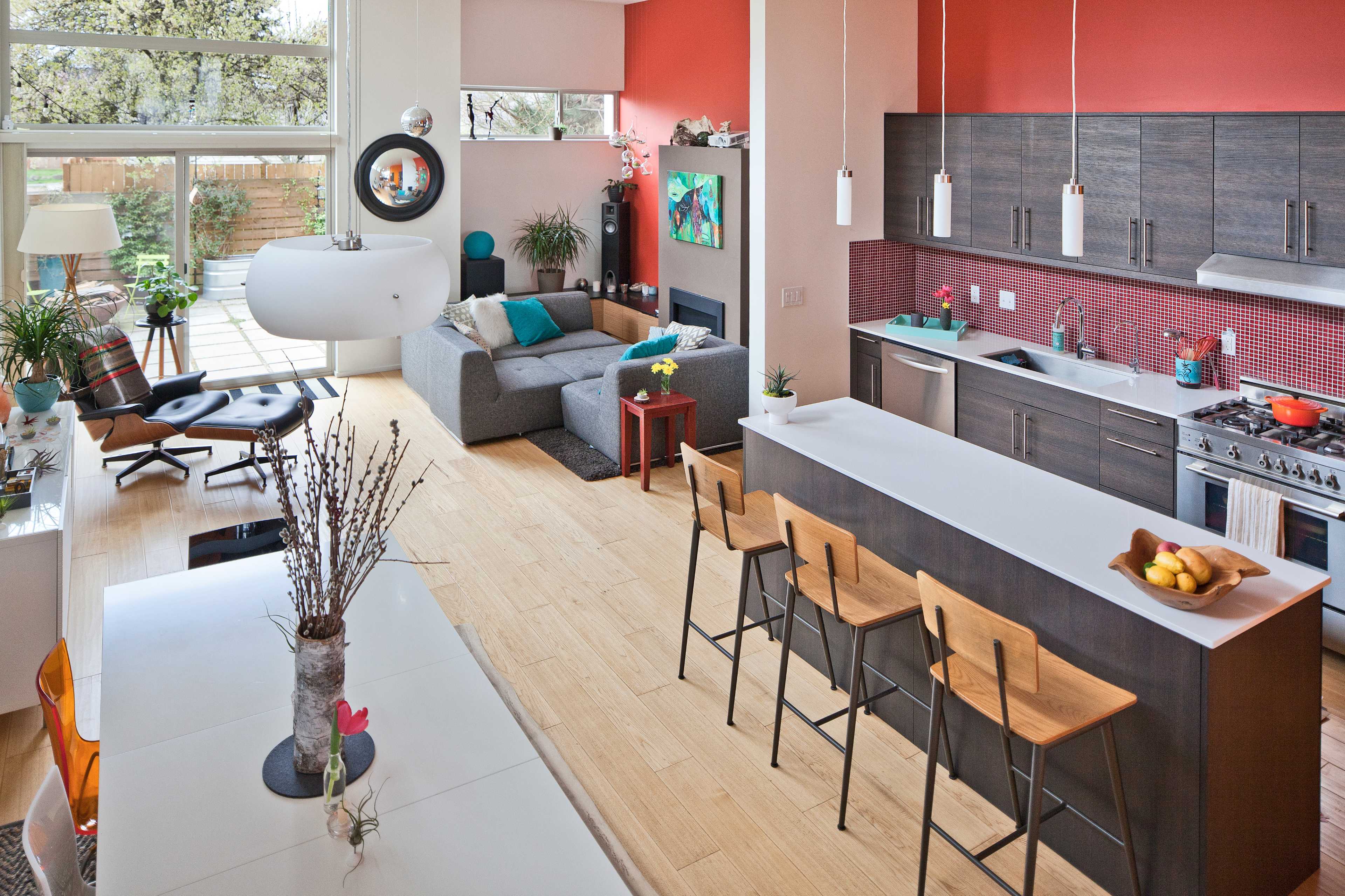 The image shows a modern, open-concept living space featuring a kitchen with a large island and dining area, adjacent to a cozy seating area with a sofa and large windows.