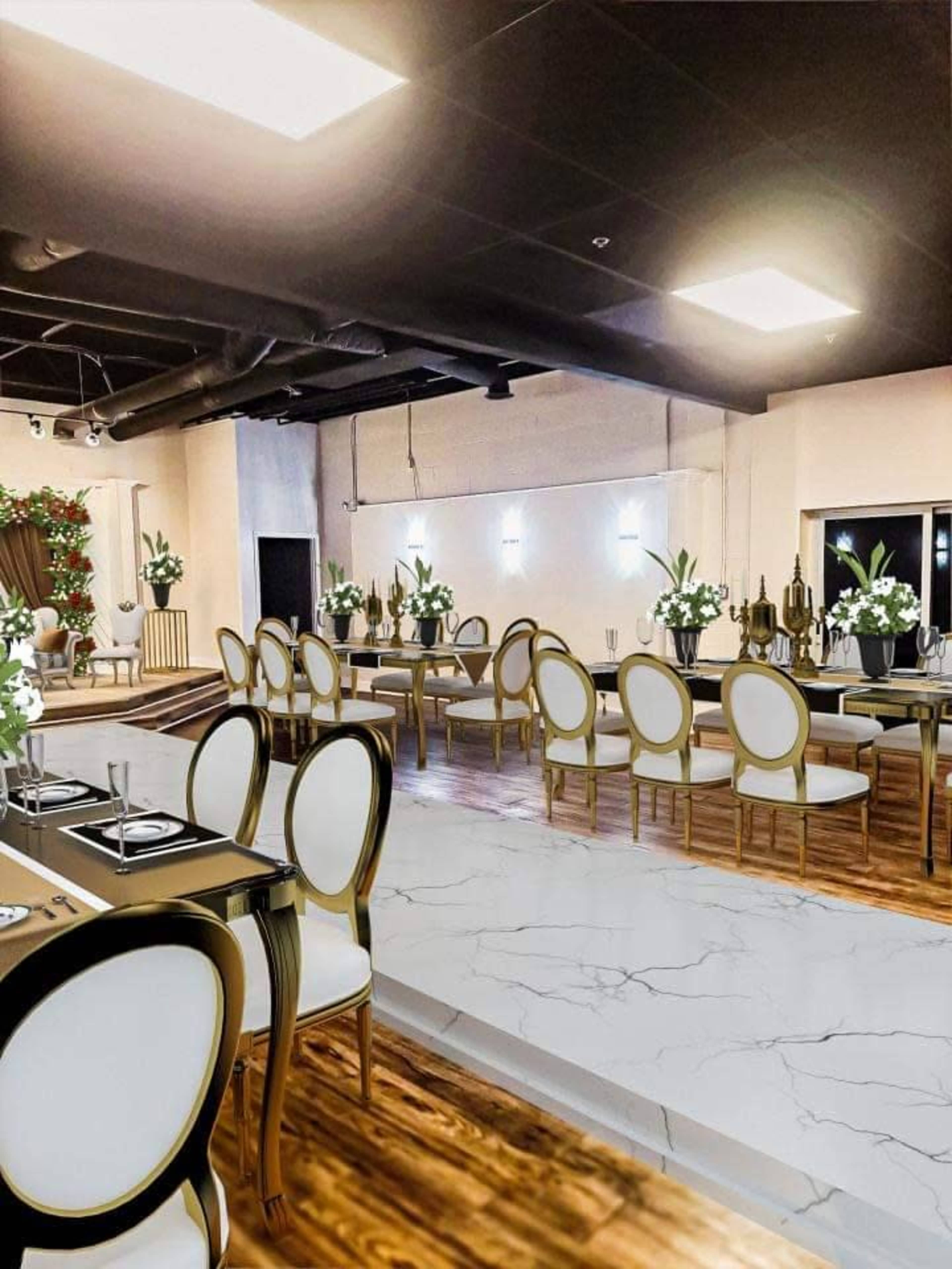 A modern dining area with tables set for a formal event, featuring elegant white and gold chairs, floral centerpieces, and a sleek floor design.