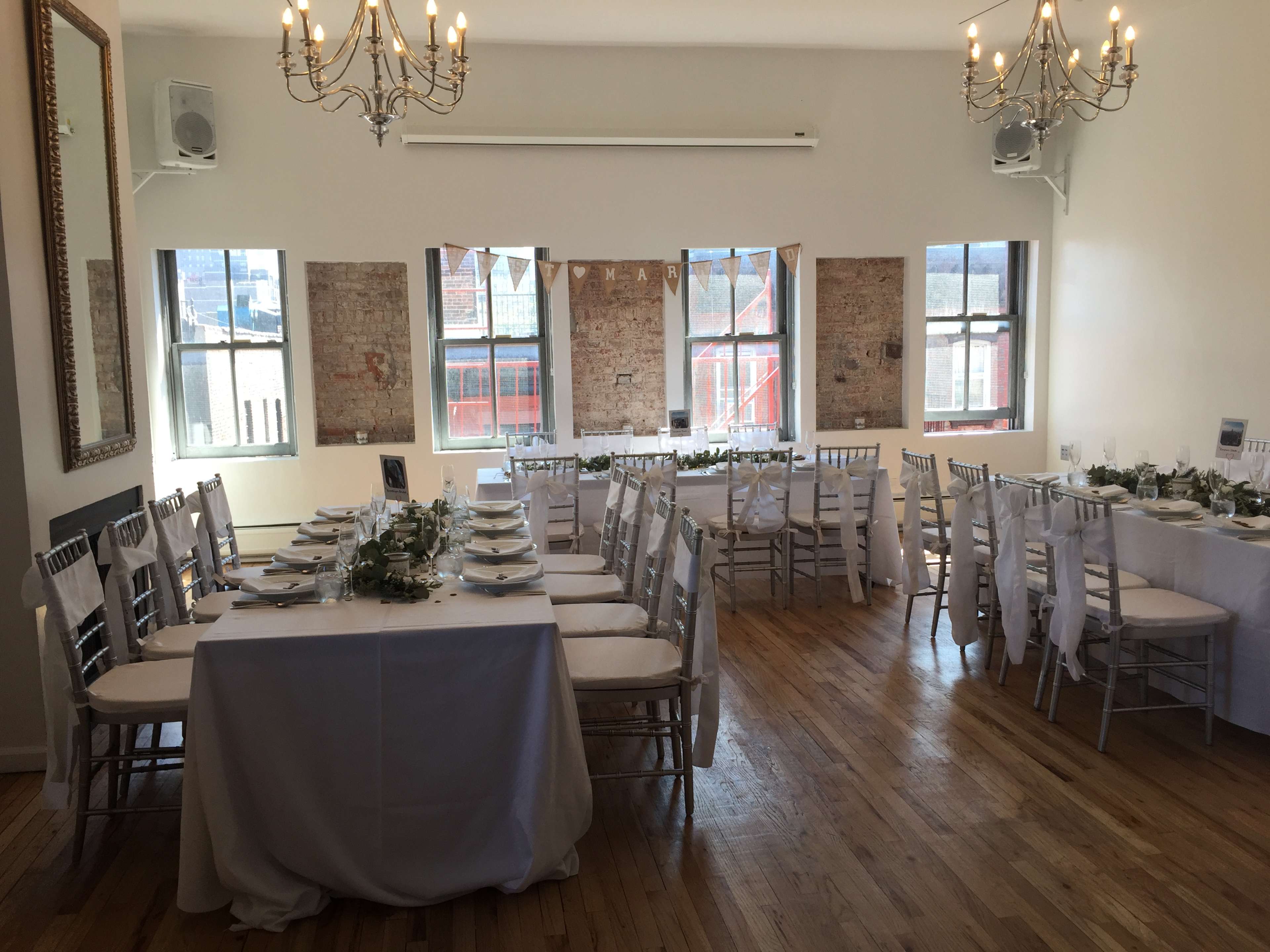 The image shows a spacious dining area arranged with long tables set for an event, complete with white tablecloths, chairs, and decorative elements.