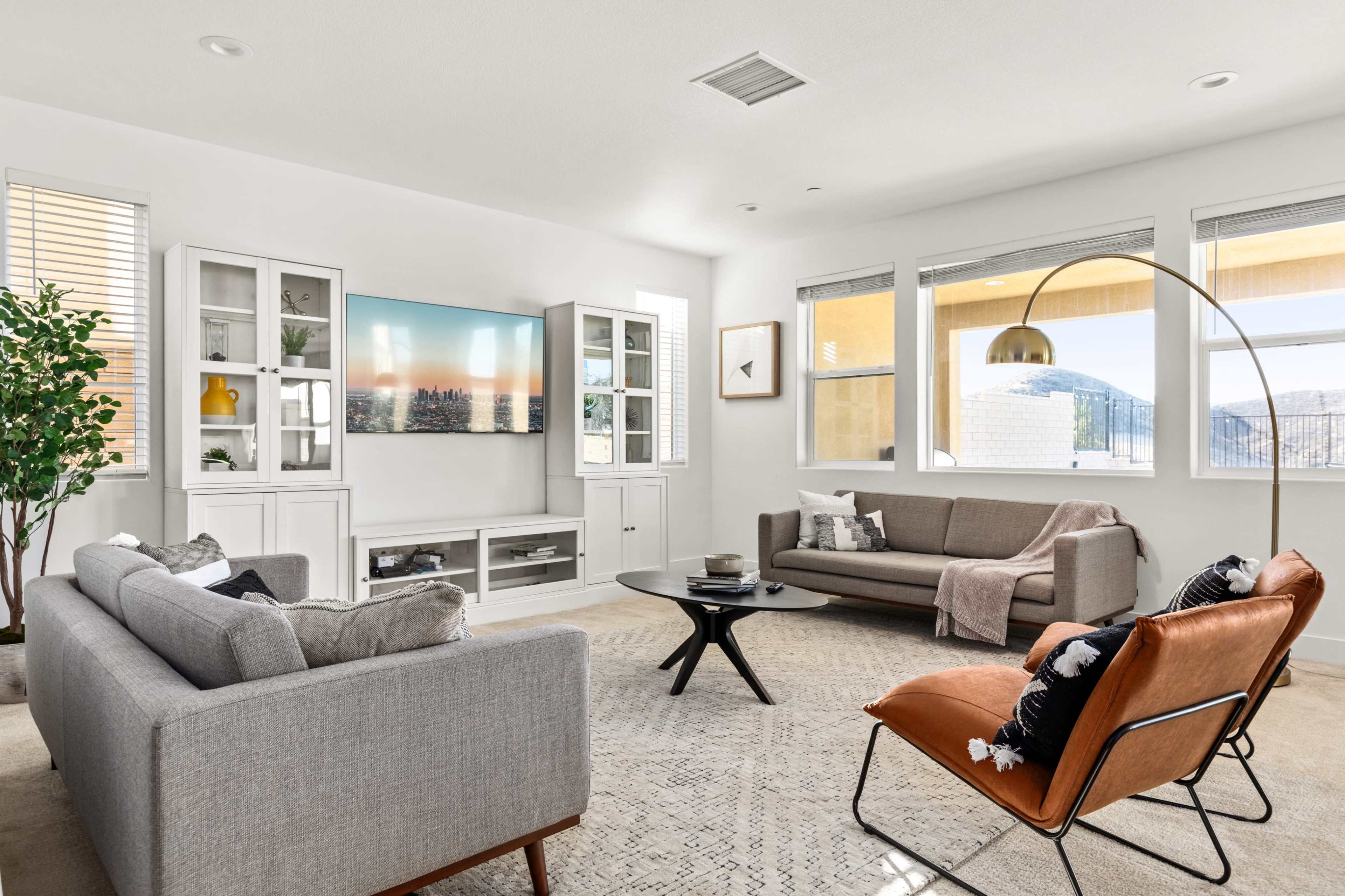 A modern living room with two sofas, a round coffee table, a large wall-mounted television, and large windows that allow natural light to enter.