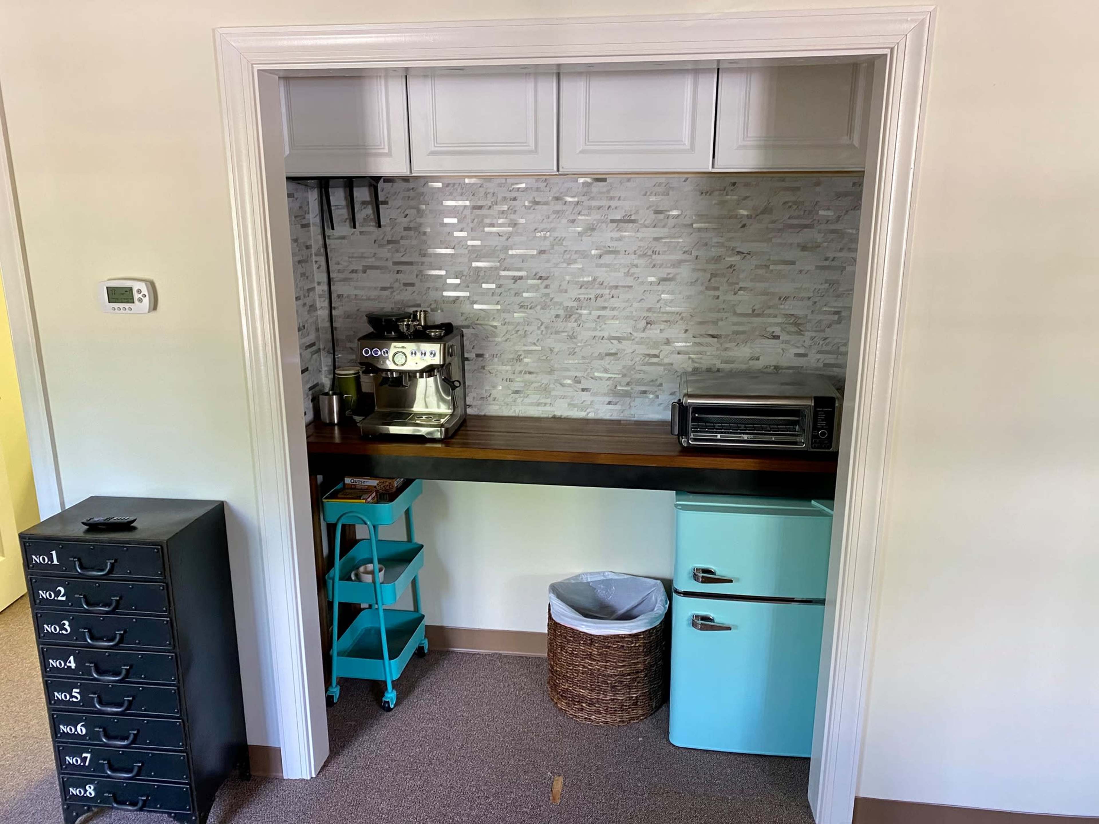A small kitchen space featuring a coffee machine, a toaster oven, a blue mini fridge, and a stack of storage drawers.