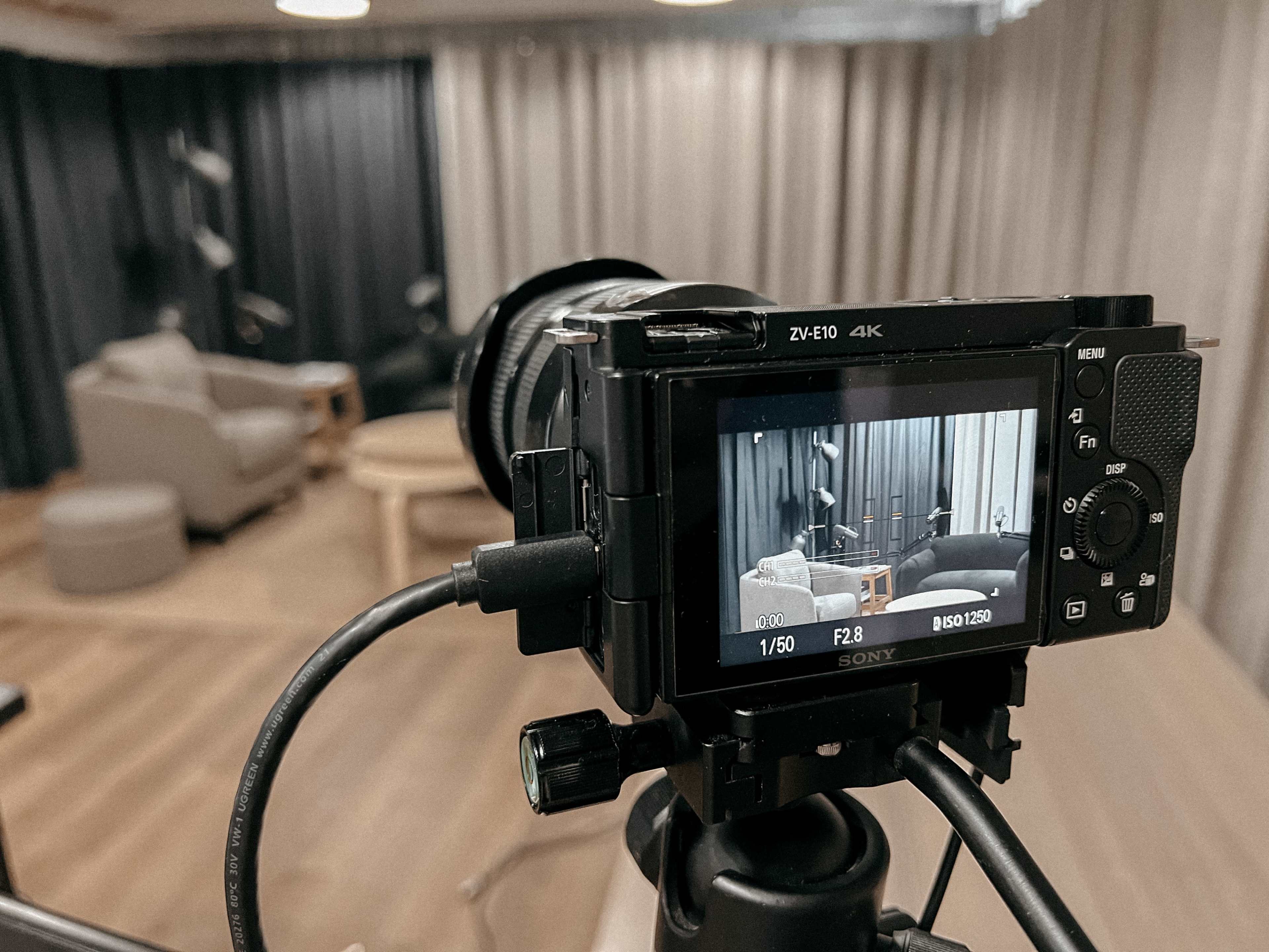 A camera is focused on a living space with a sofa, an armchair, and a coffee table, surrounded by curtains.