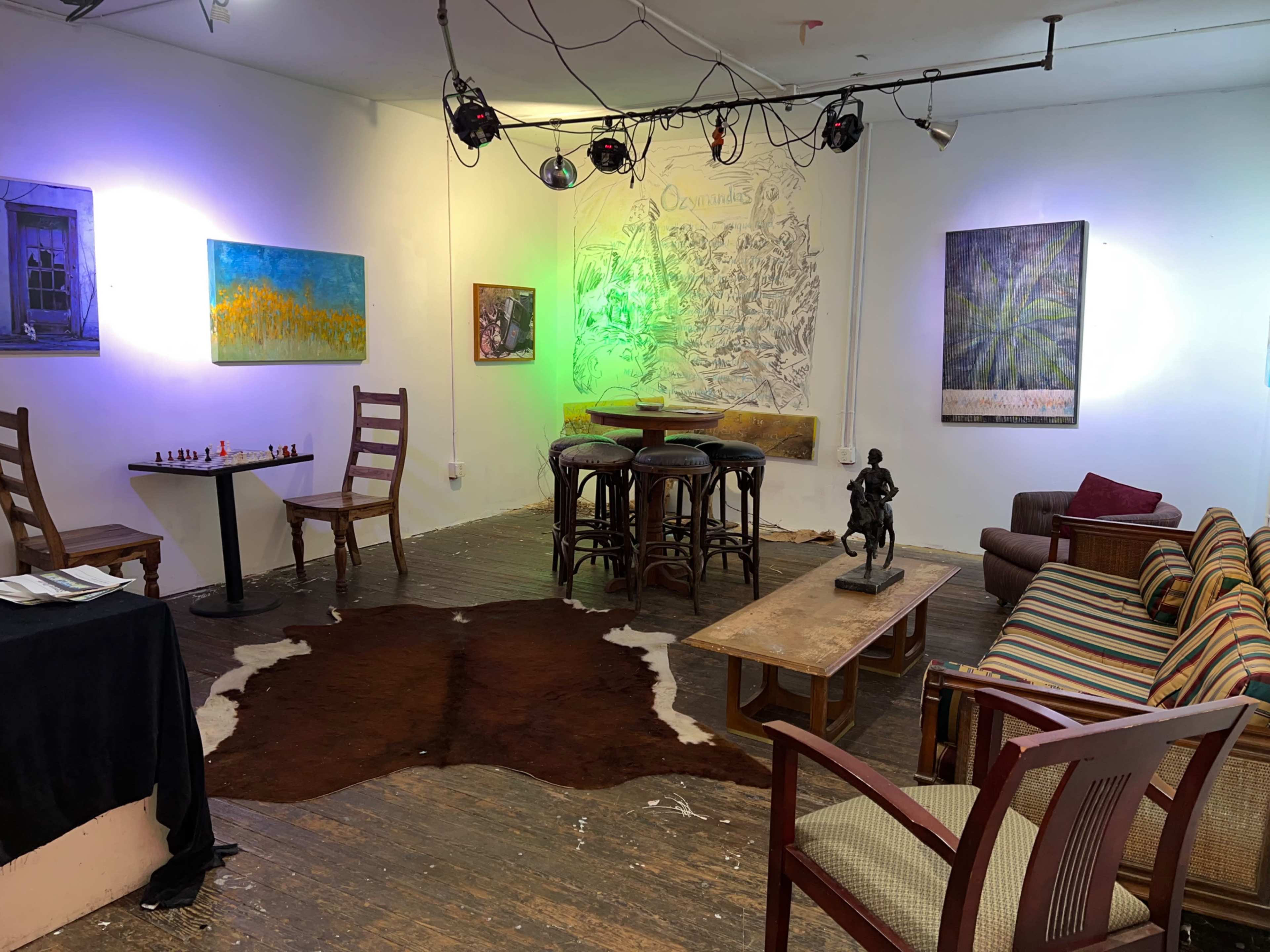 The scene shows an art gallery with a seating area, a chess table, and several paintings on the walls, illuminated by colorful lights.