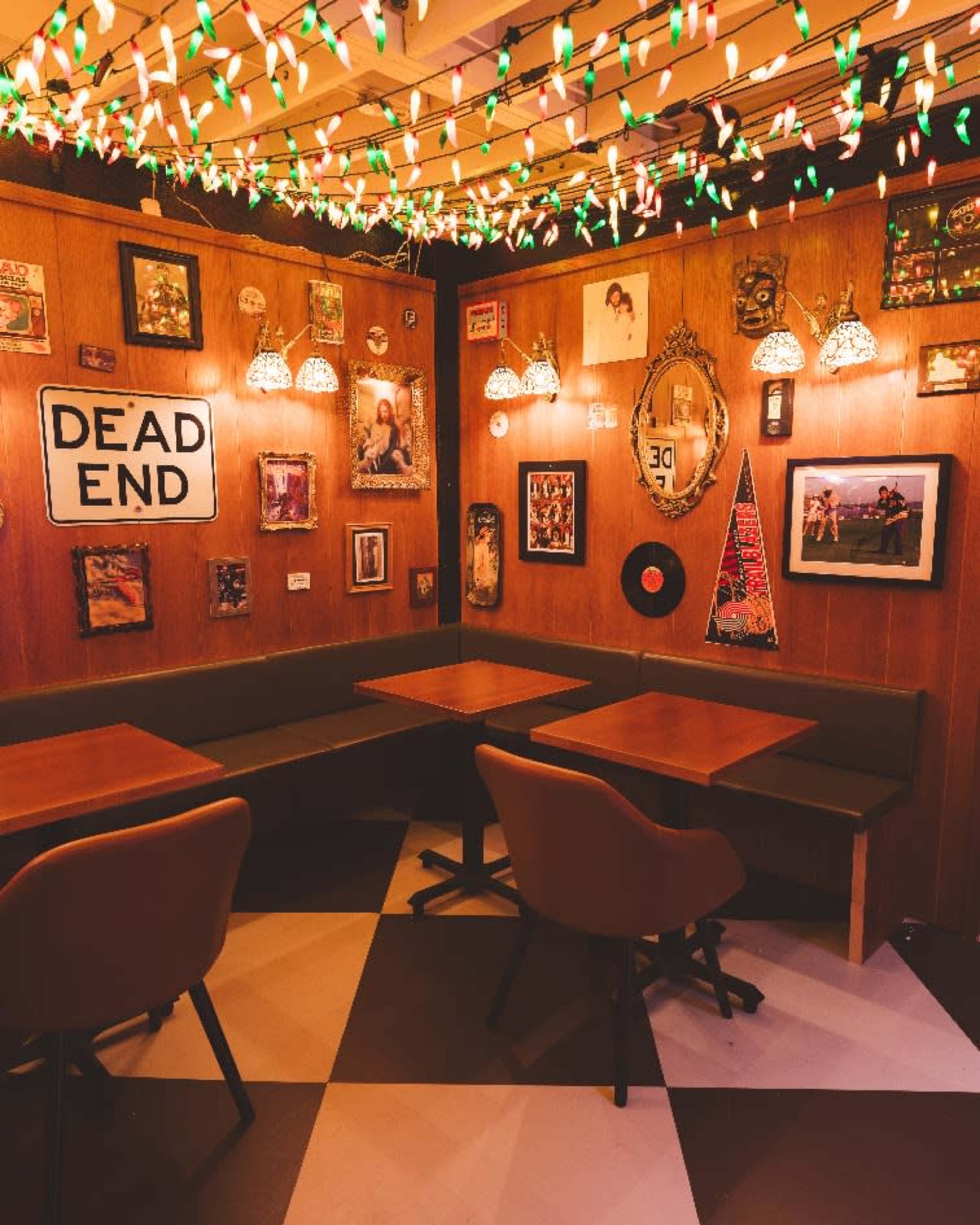 A cozy corner of a restaurant features wooden walls adorned with framed pictures and vintage decor, illuminated by string lights and pendant lamps.