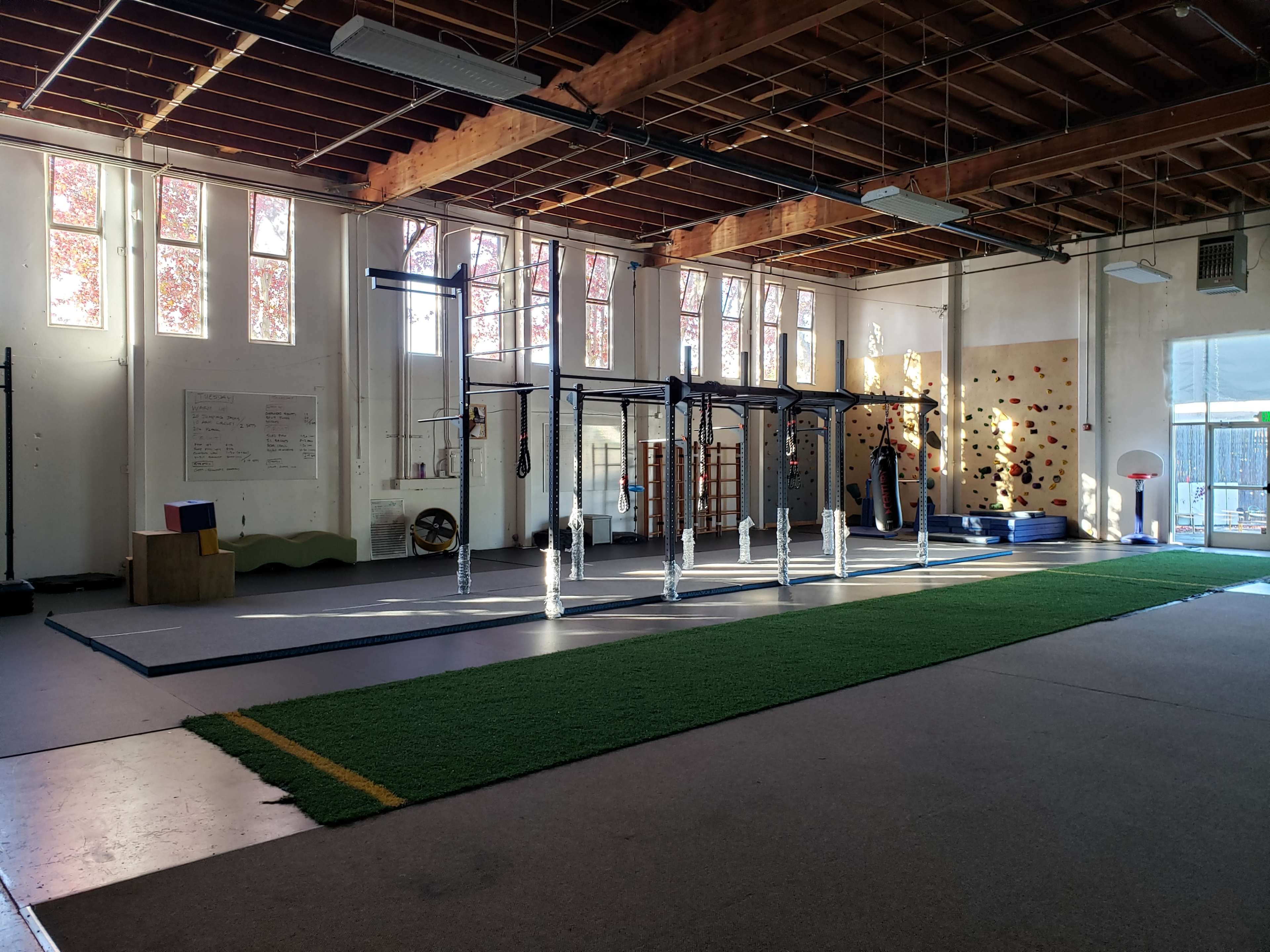 An empty gymnasium with exercise equipment, large windows, and a climbing wall.