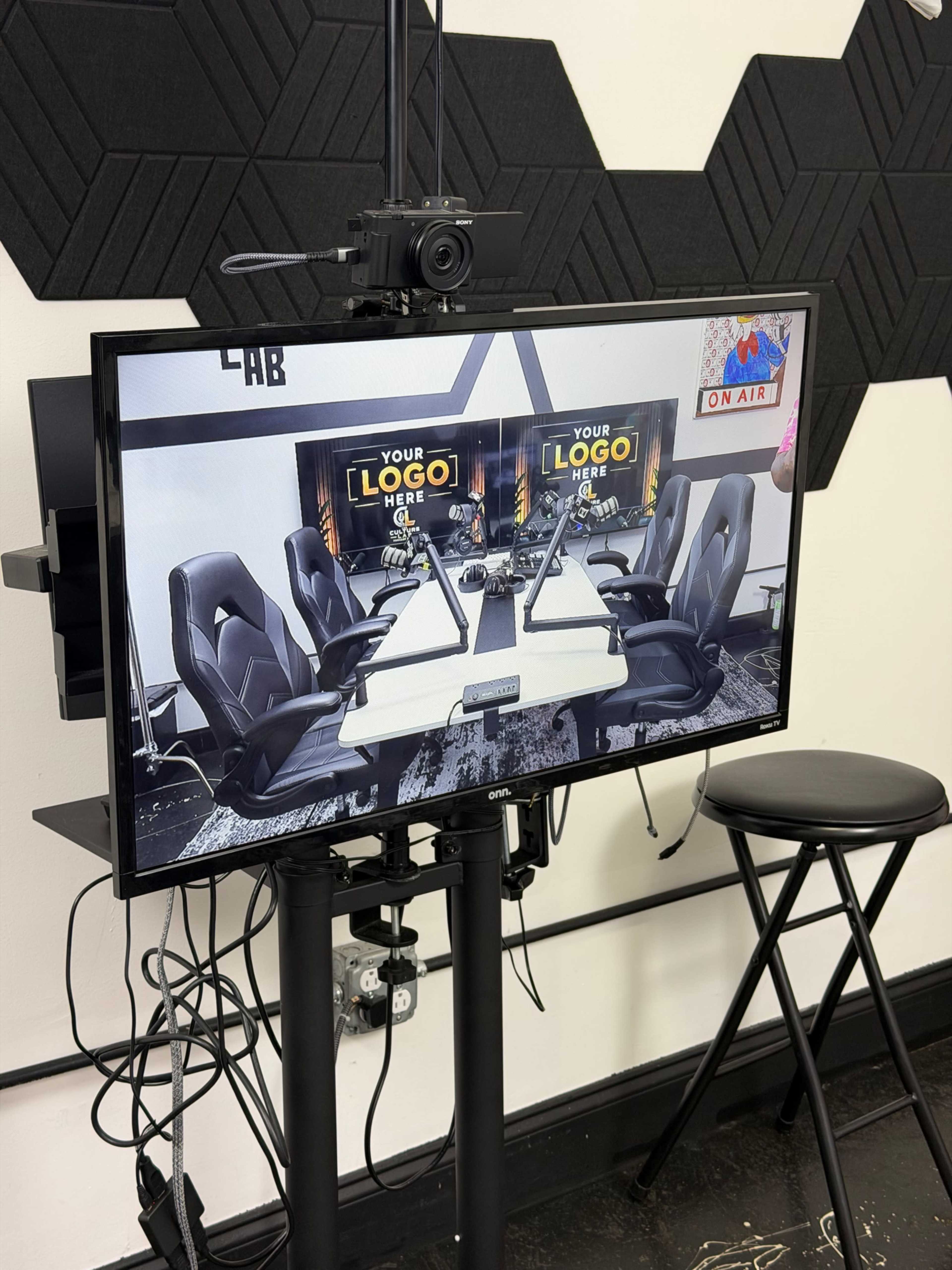 The image shows a camera setup focused on a monitor displaying an empty conference room with chairs and a sign for logo placement.