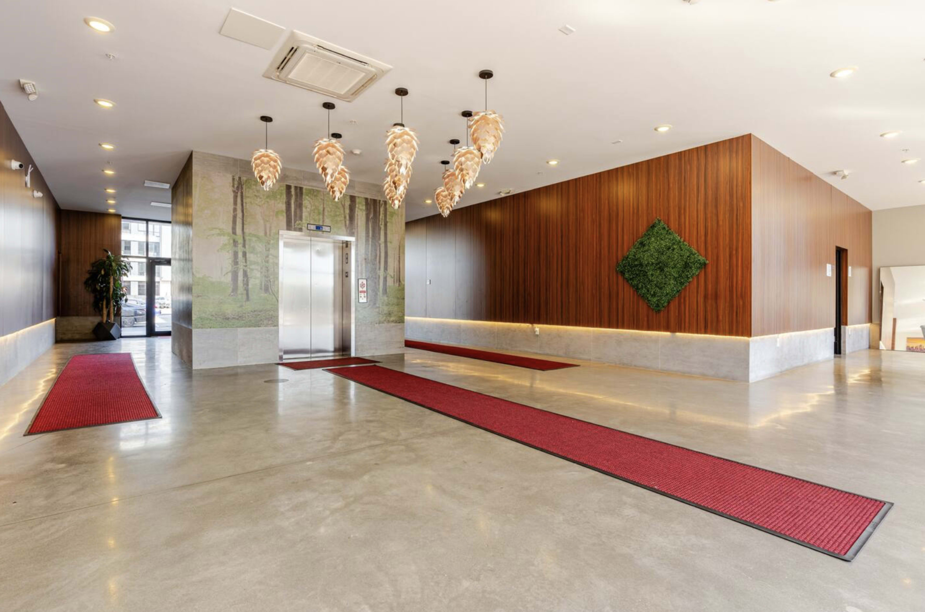 The image depicts a modern lobby with a polished concrete floor, red runners, an elevator, and decorative pendant lights.