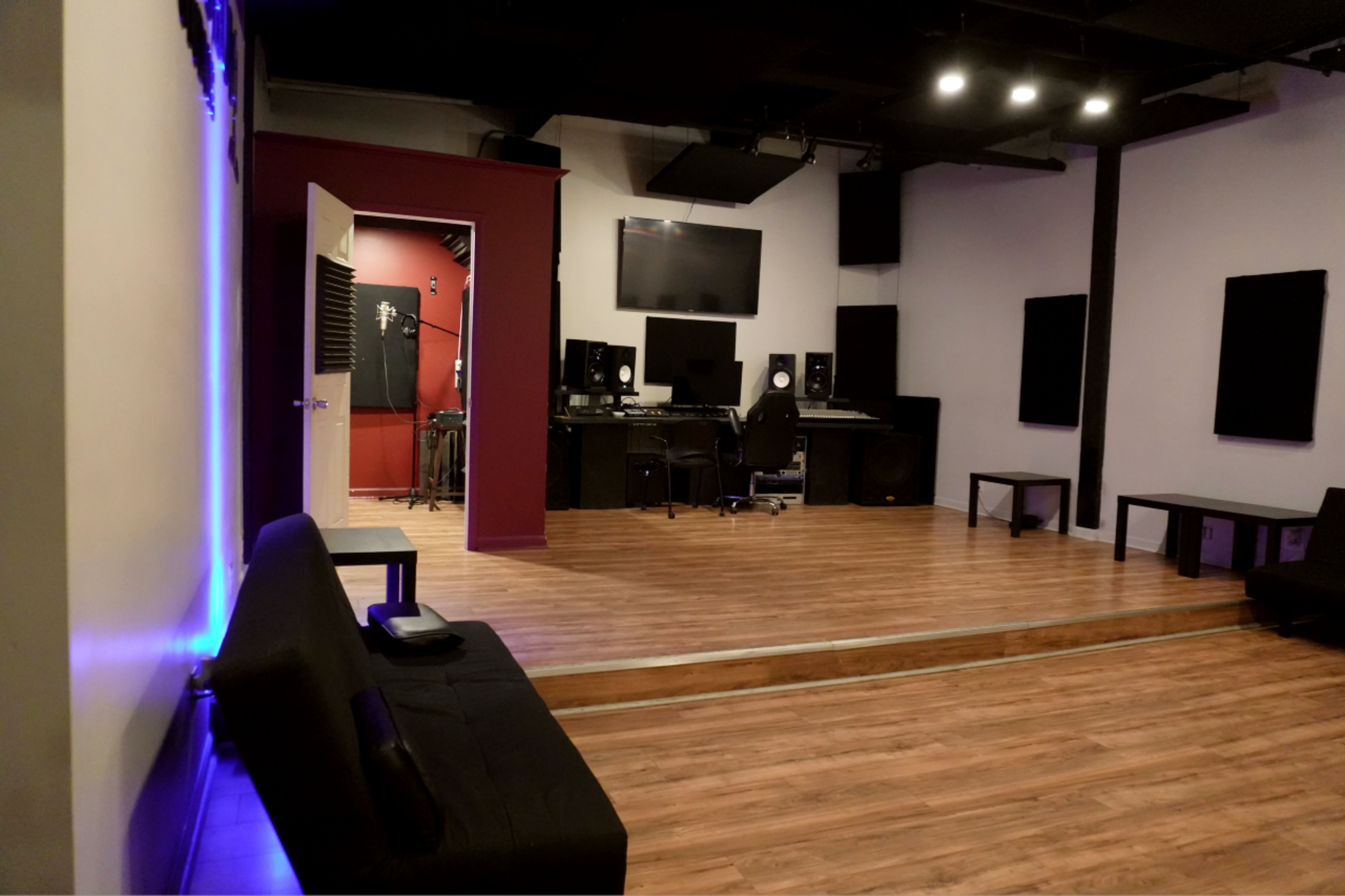 A recording studio with wooden flooring, a control desk, speakers, and soundproofed walls.
