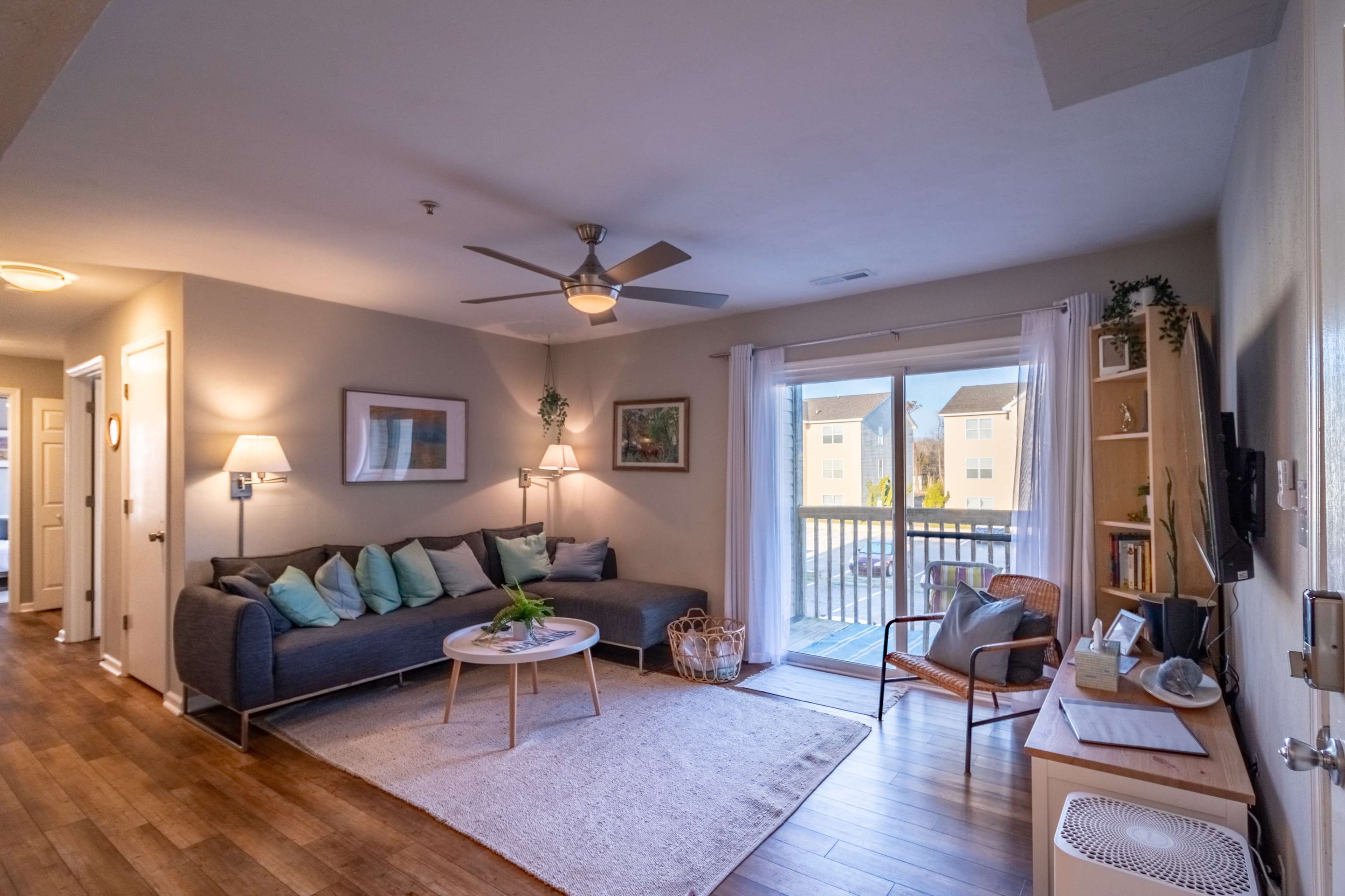 A modern living room features a gray sofa, a round coffee table, and sliding glass doors leading to a patio, with wooden flooring throughout.