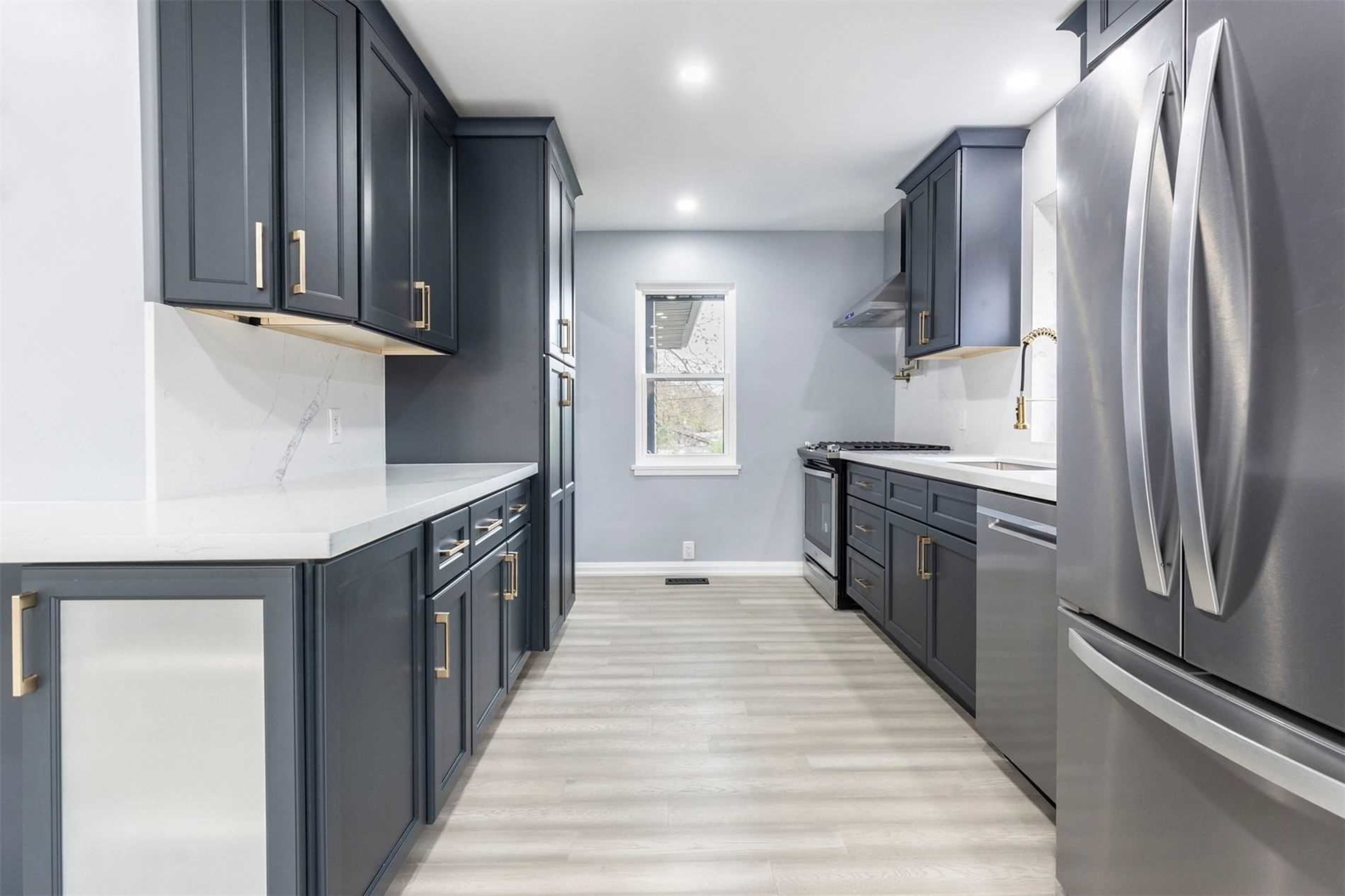 A modern kitchen features dark blue cabinetry, stainless steel appliances, and light-colored countertops with a simple design.
