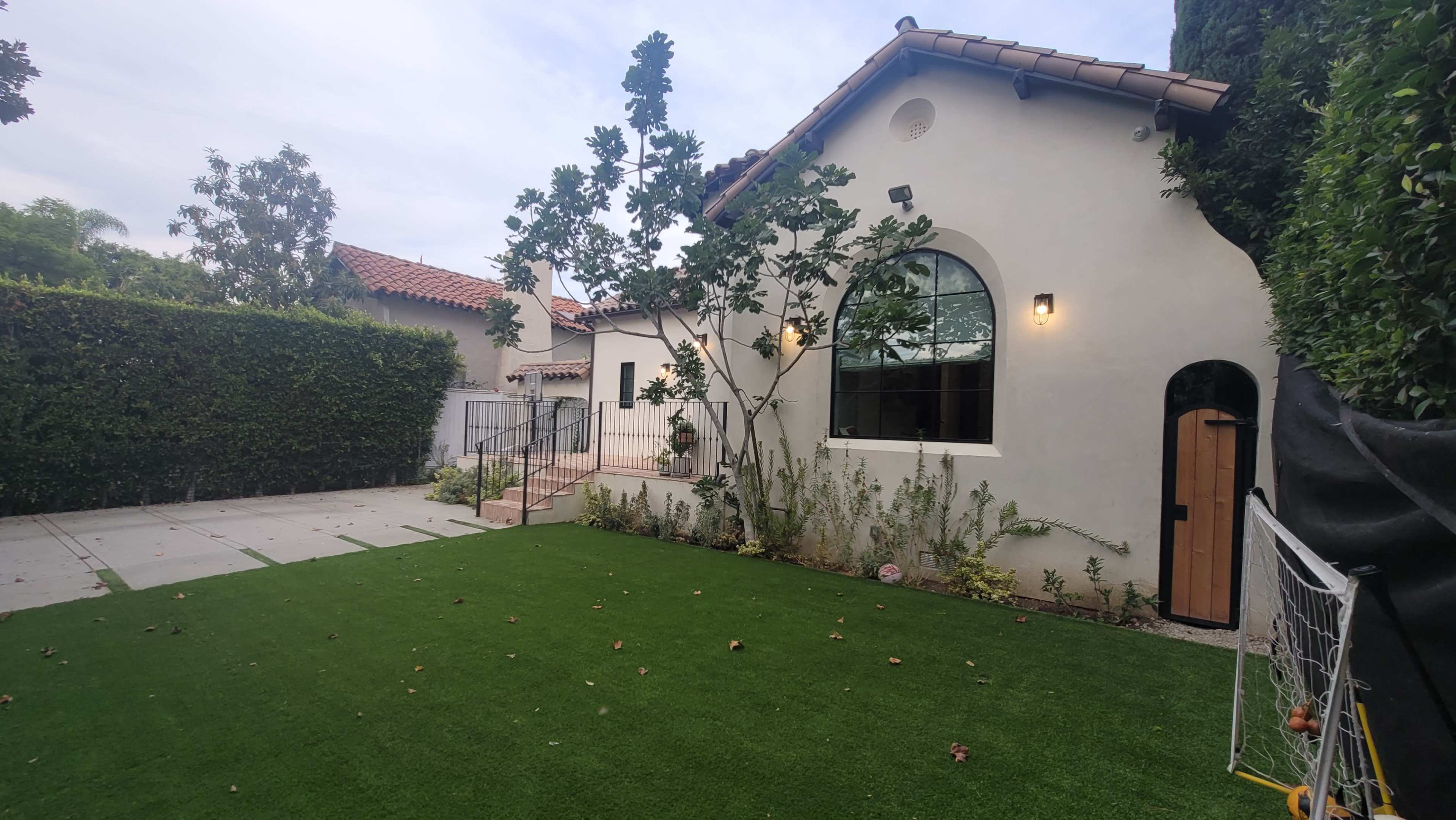 A landscaped backyard features a well-maintained lawn, a house with a tiled roof, and surrounding greenery.