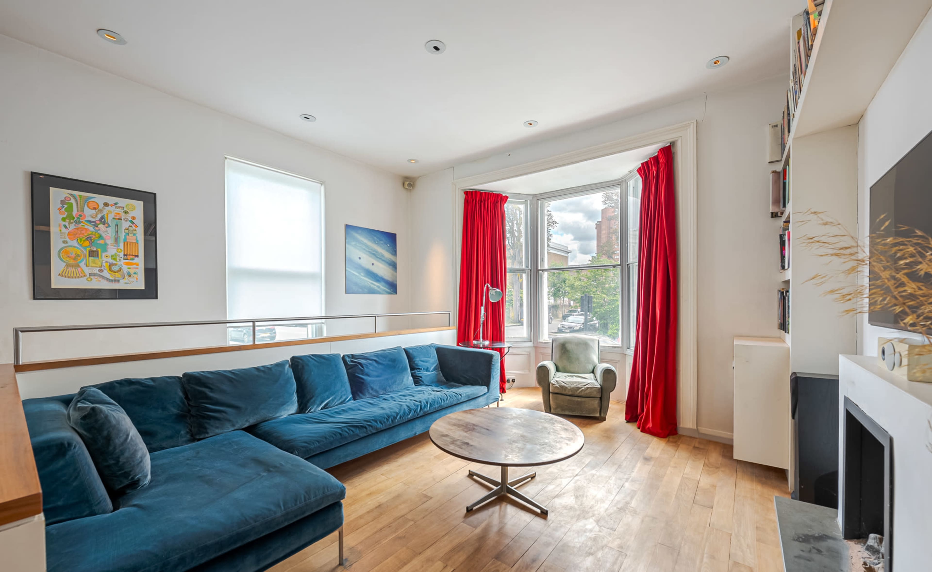 A living room featuring a blue sectional sofa, a round coffee table, and large windows with red curtains.