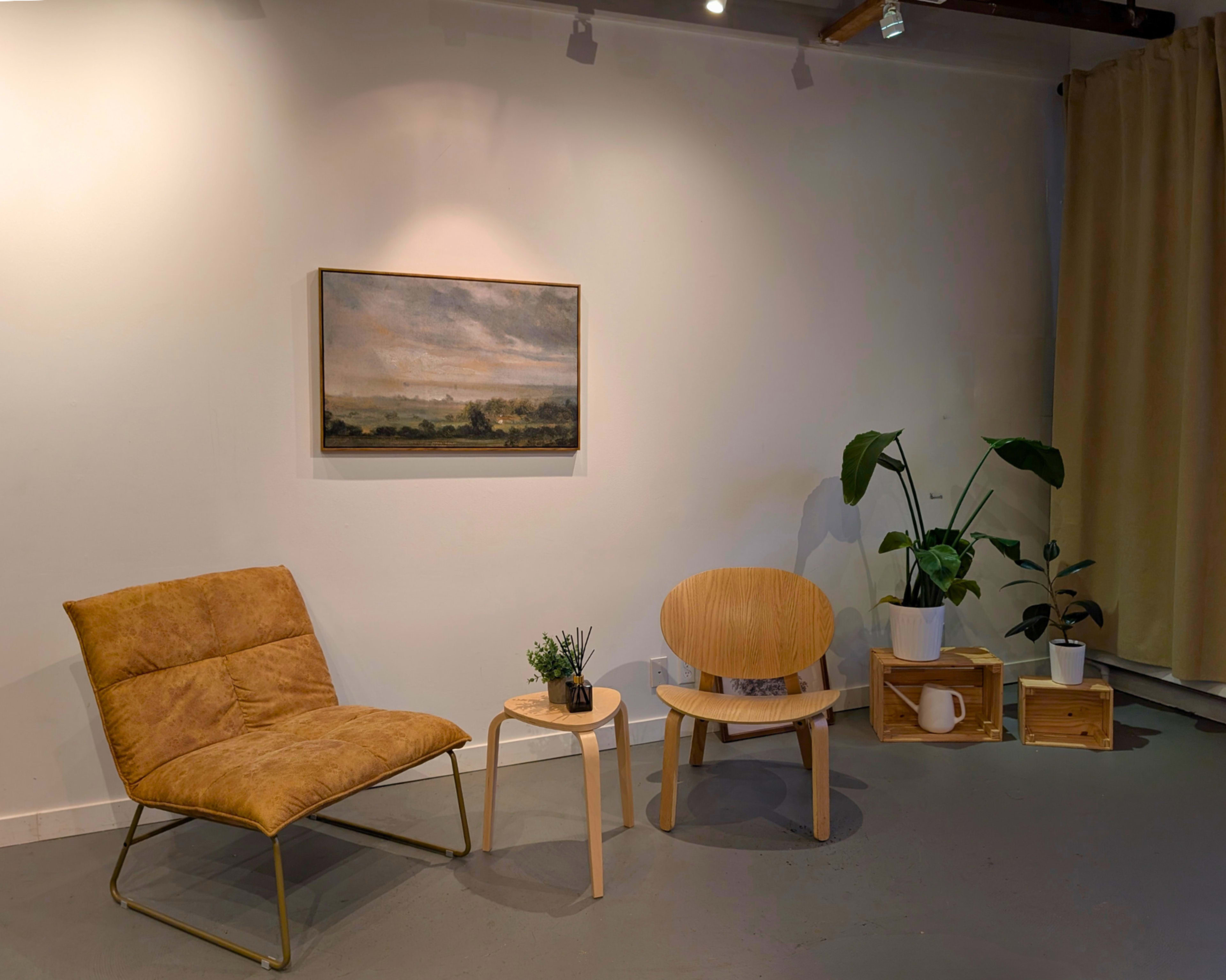 The image depicts a minimalist room with two stylish chairs, a small table, a potted plant, and a painting on the wall.