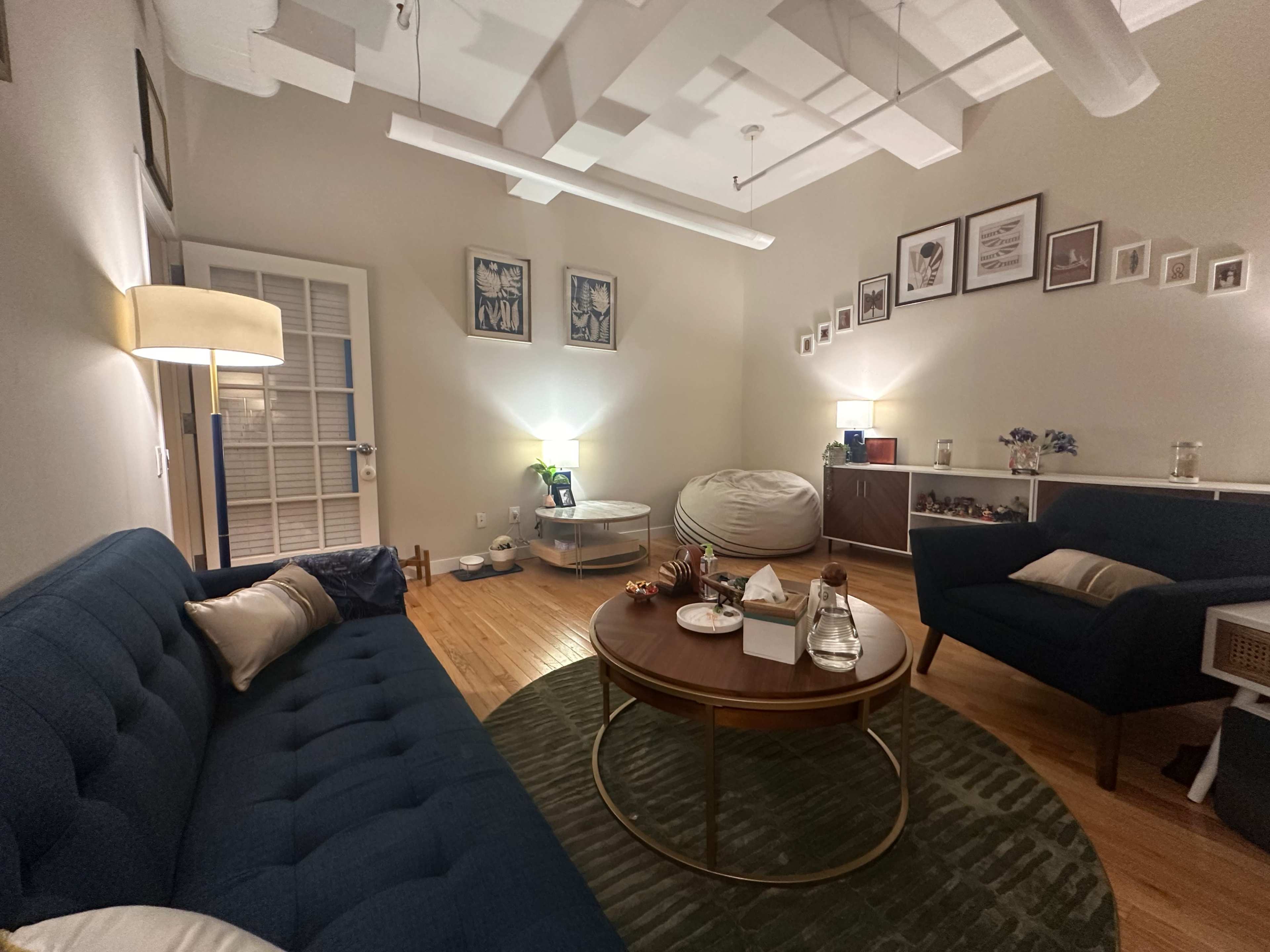 The image depicts a cozy living room with a blue sofa, a round coffee table, and a small seating area, featuring soft lighting and decorative wall frames.