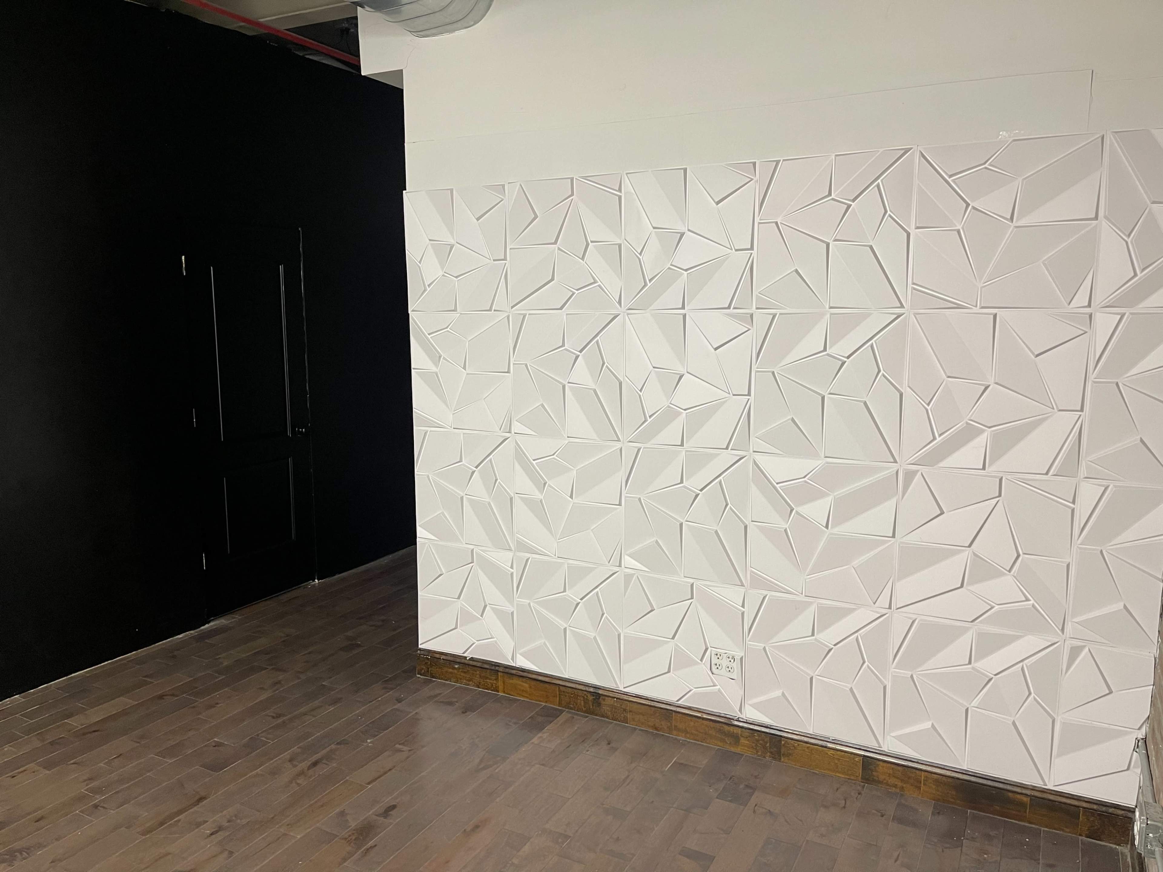 A modern interior with a textured white wall on one side and a black wall with a door on the other.