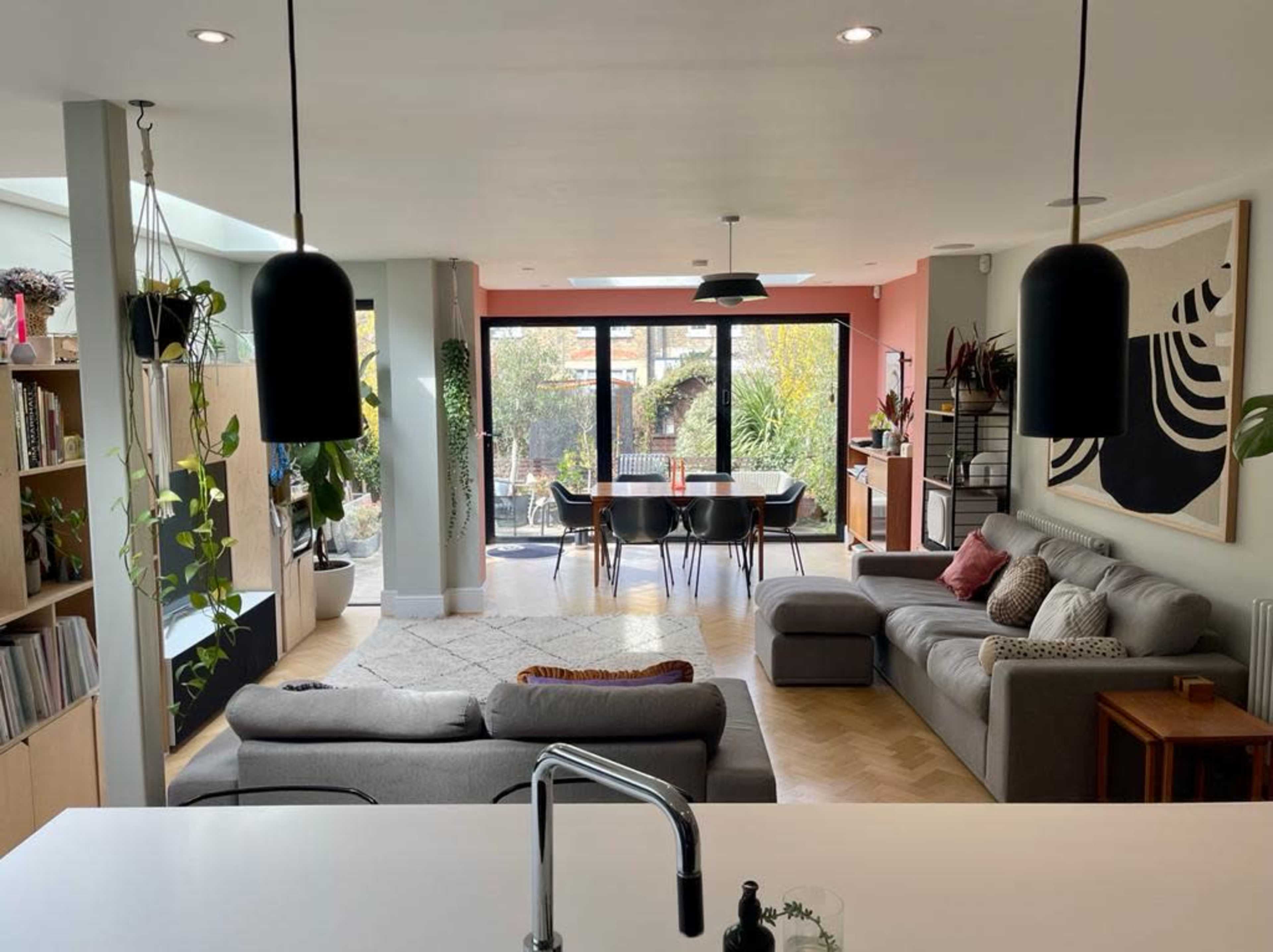 A modern living room and dining area with large windows, a sofa, a dining table, and various plants.