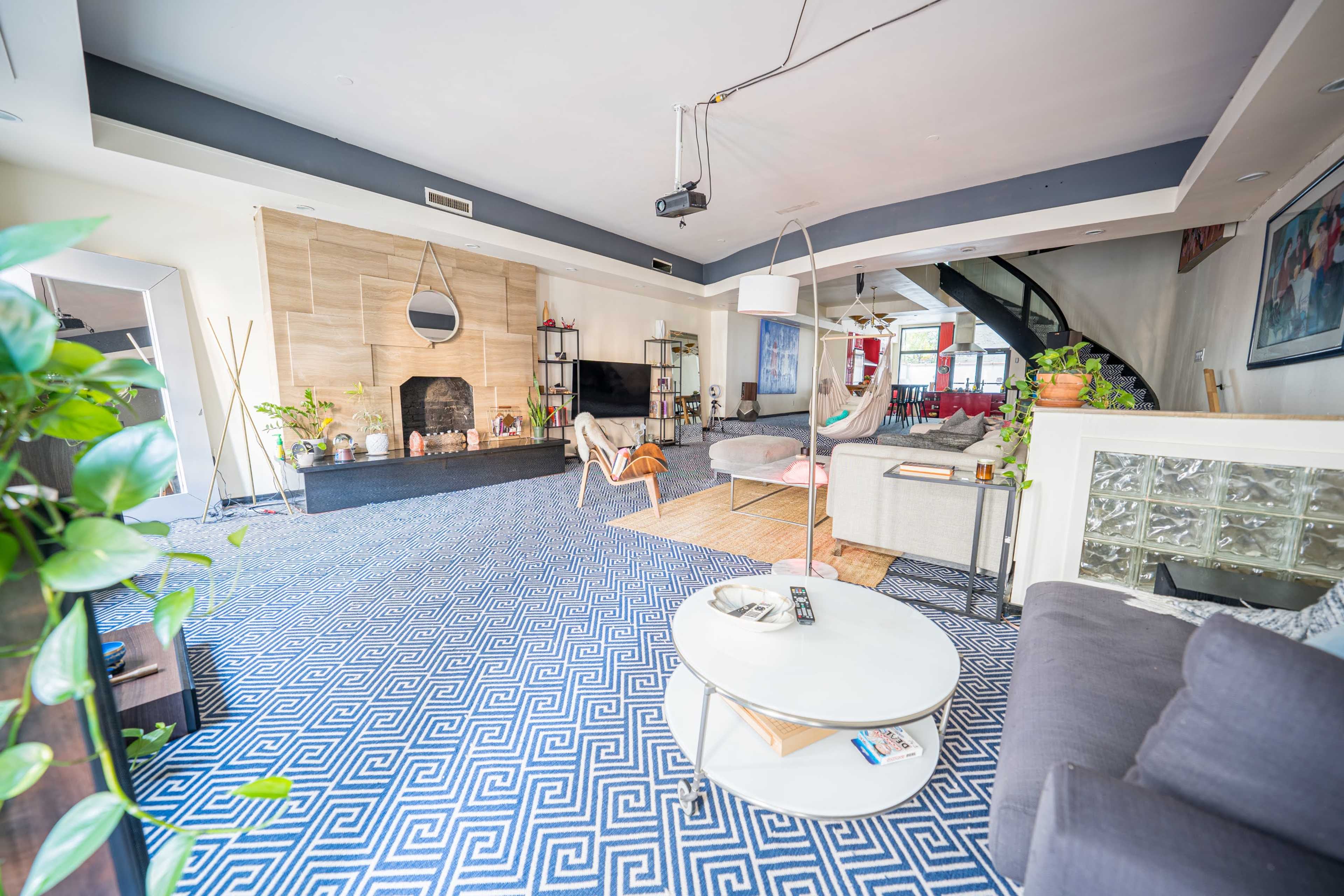 A spacious, modern living room with a blue patterned rug, a fireplace, and a staircase leading to another level.