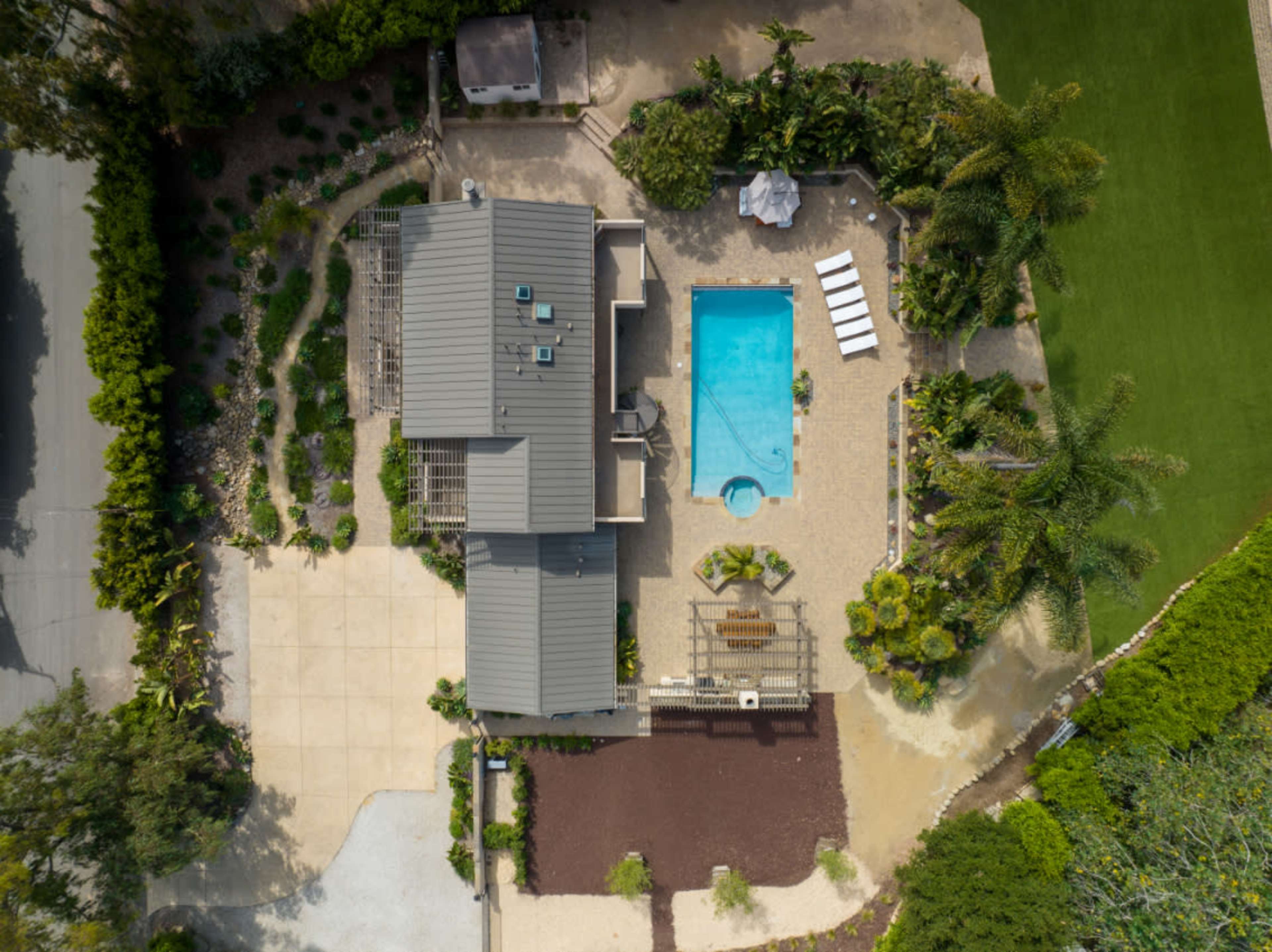 An aerial view of a house with a pool, surrounded by landscaped gardens and a driveway.