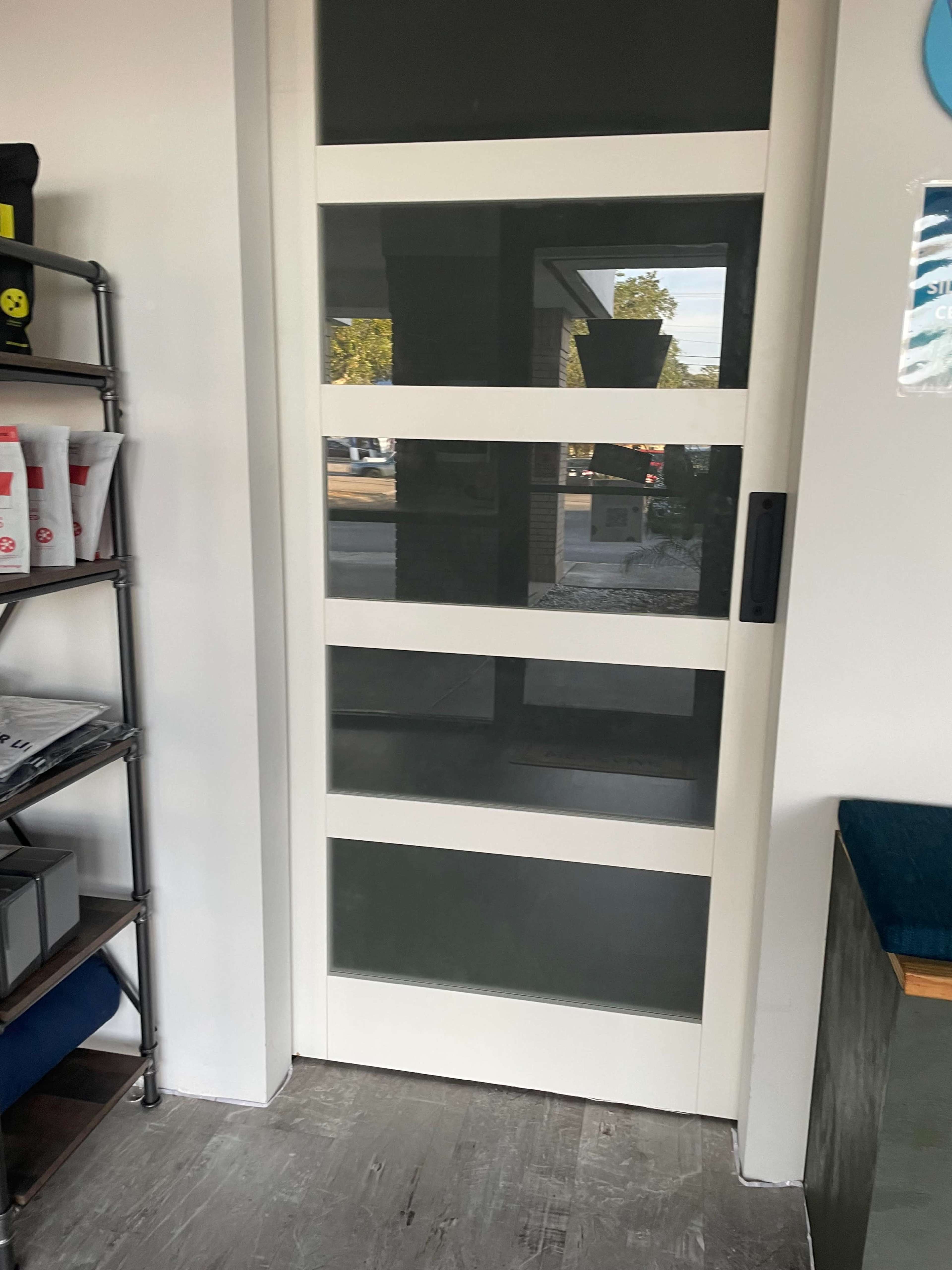 The image shows a white sliding door with four horizontal glass panels, set in an interior space.