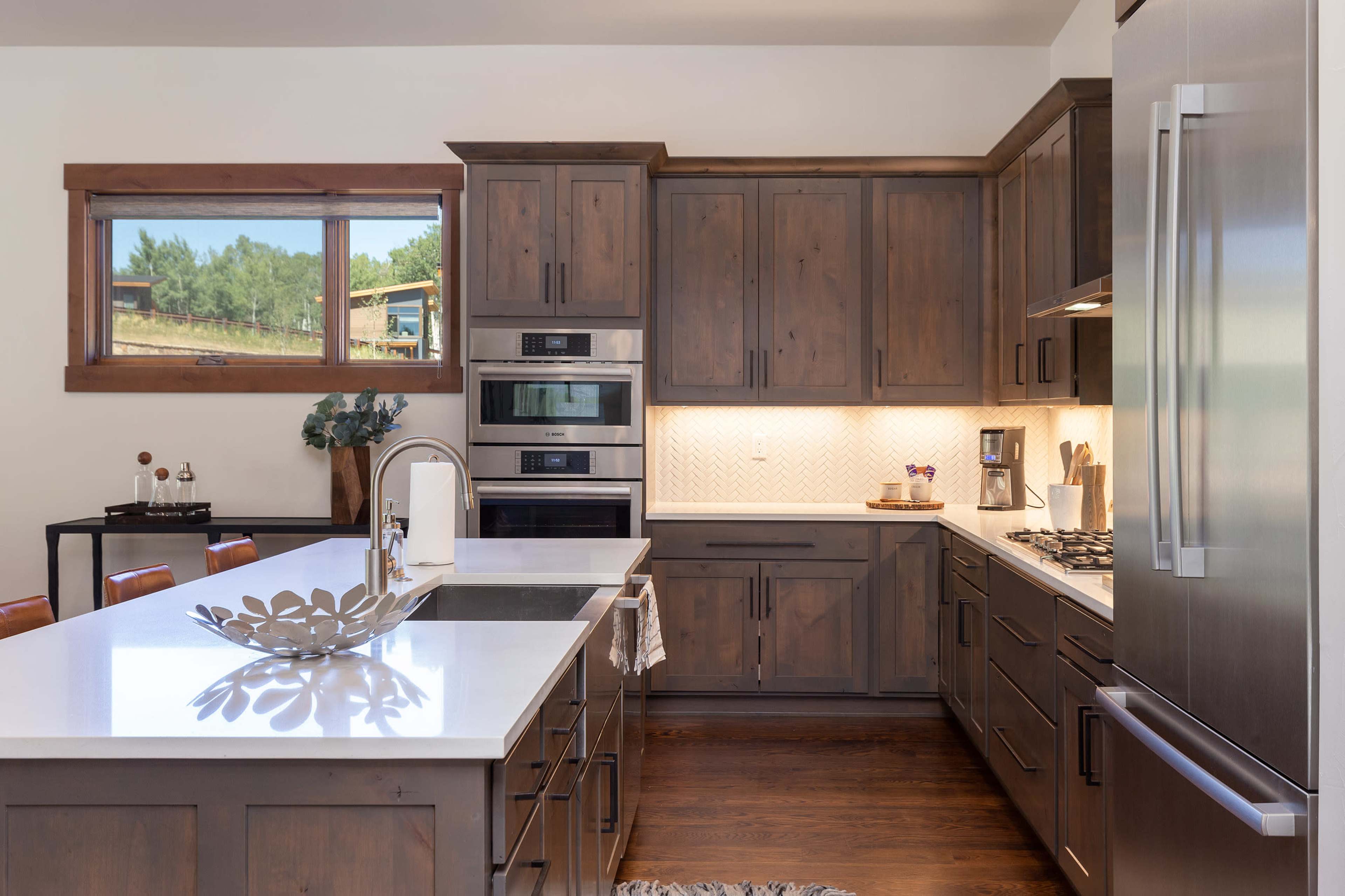 A modern kitchen with wooden cabinets, stainless steel appliances, and a large island topped with a white countertop.