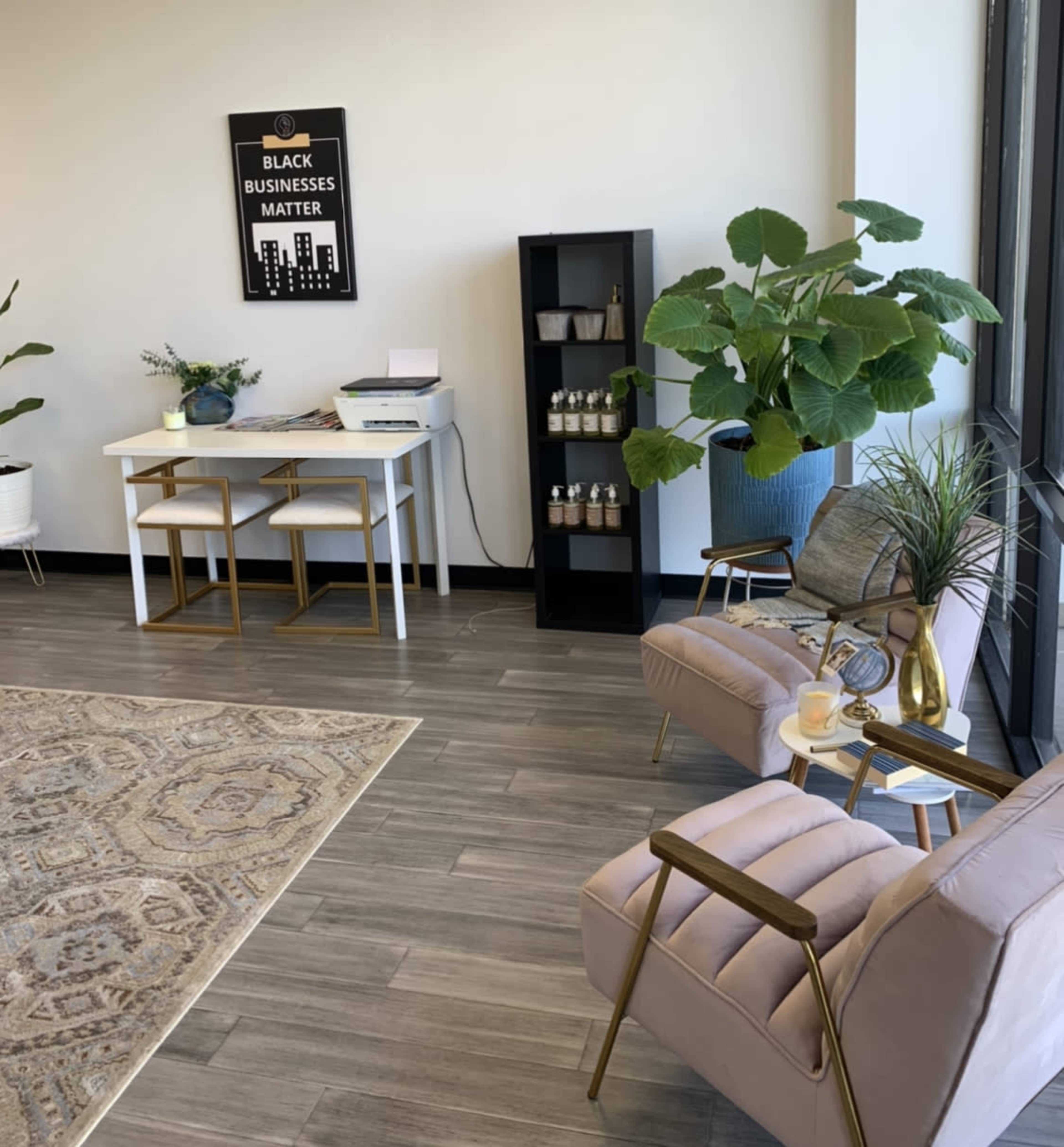 A modern office space with a table and chairs, a printer, a bookshelf, and two upholstered armchairs beside a decorative plant.