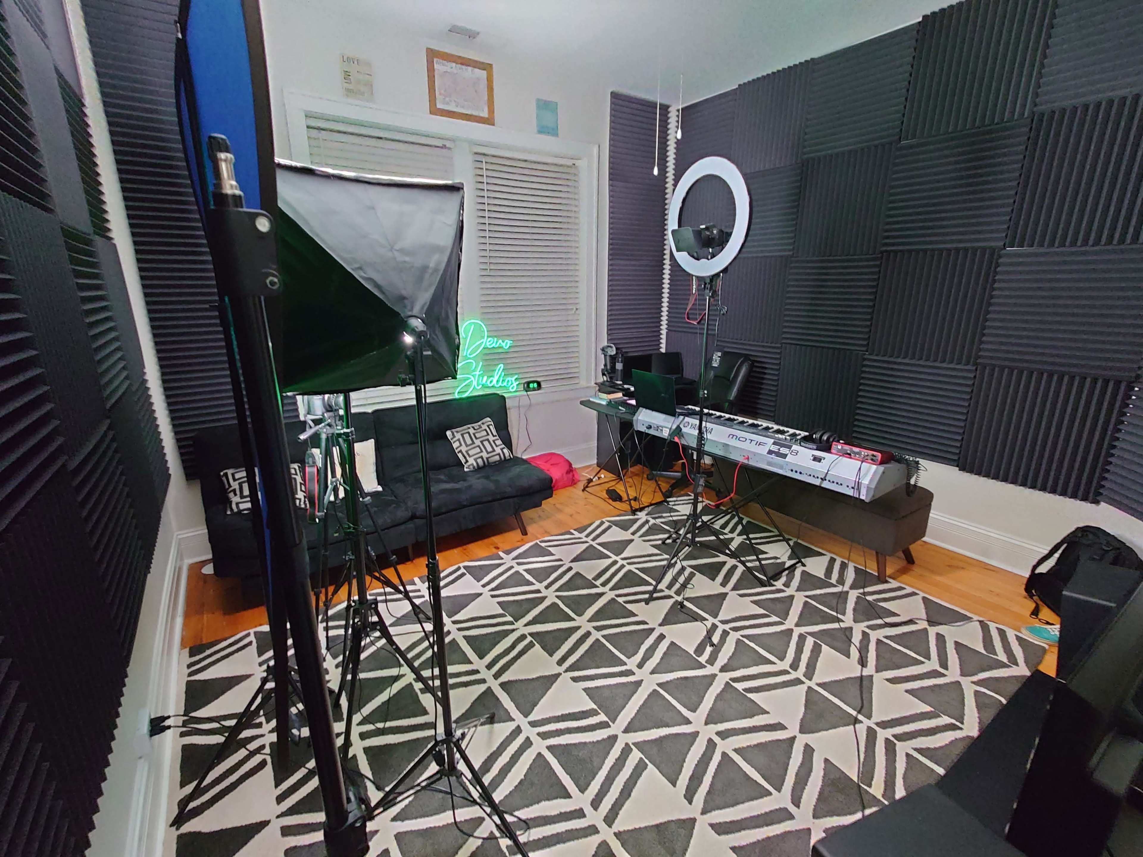 A music studio with soundproofing foam on the walls, a keyboard setup, lighting equipment, and a patterned rug.