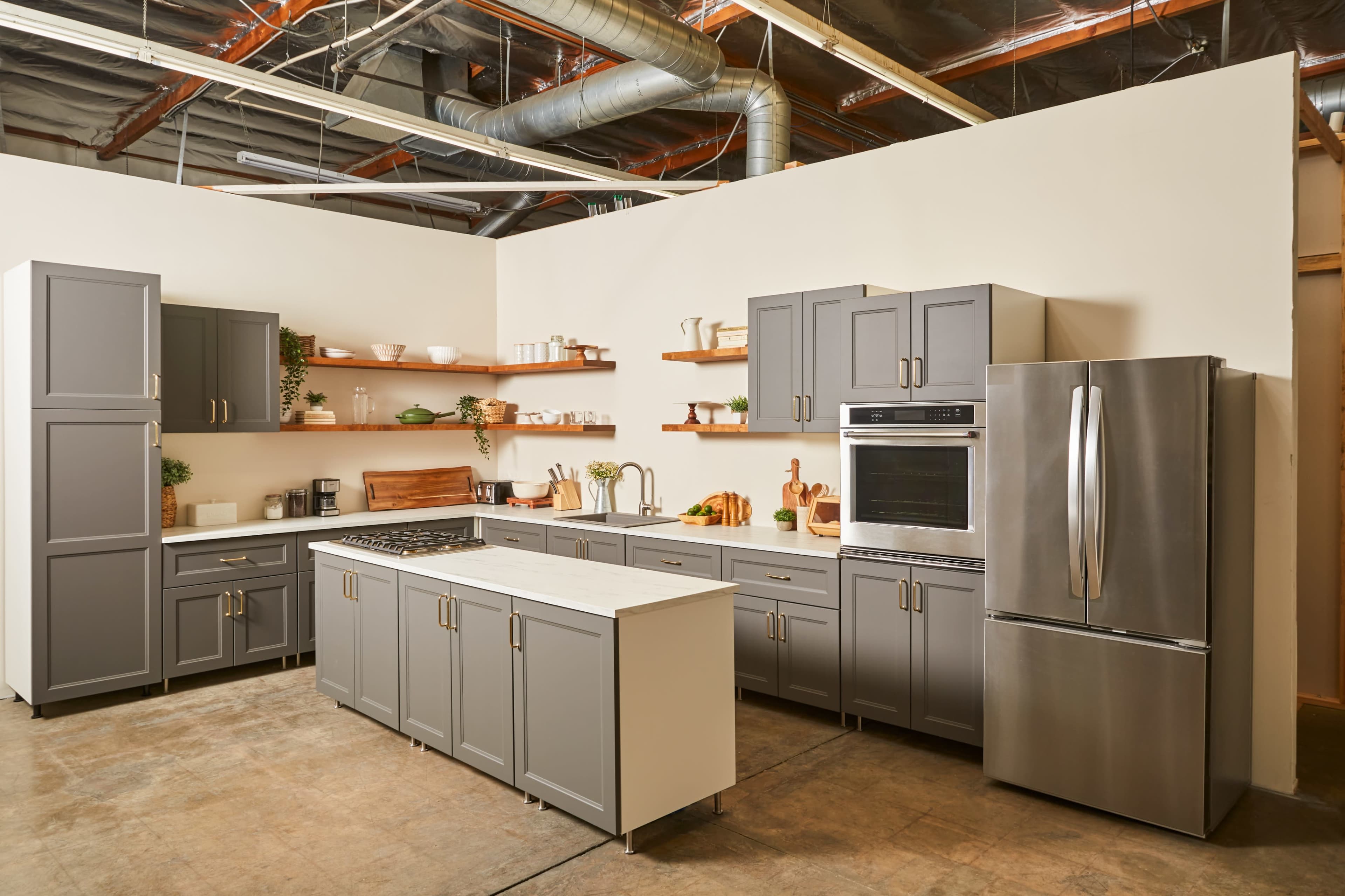 A modern kitchen features gray cabinets, a stainless steel refrigerator, a gas stove, and open shelves displaying various kitchenware.