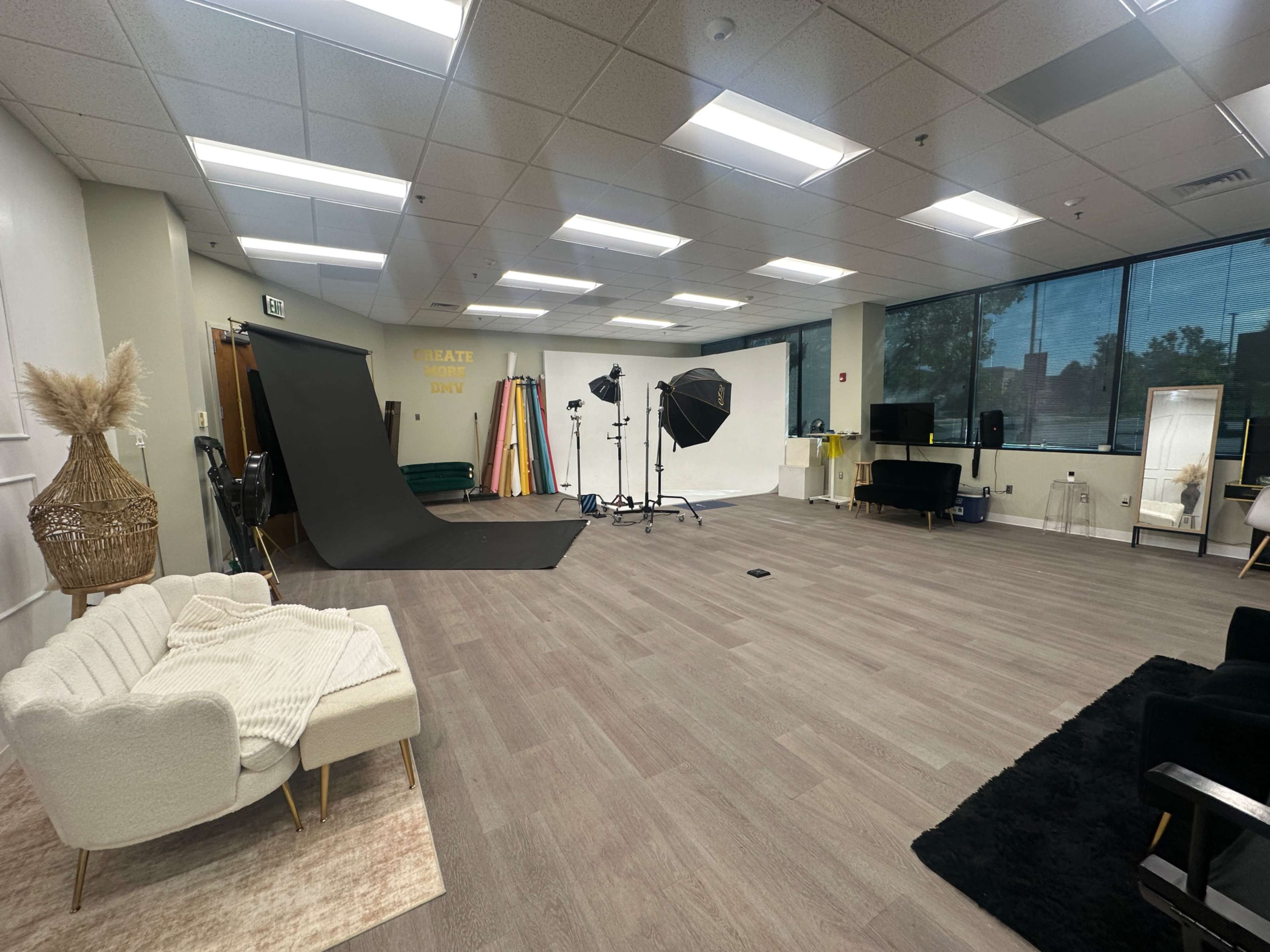 The image shows a spacious photography studio with a black backdrop, soft seating area, and multiple colored backdrops on display.