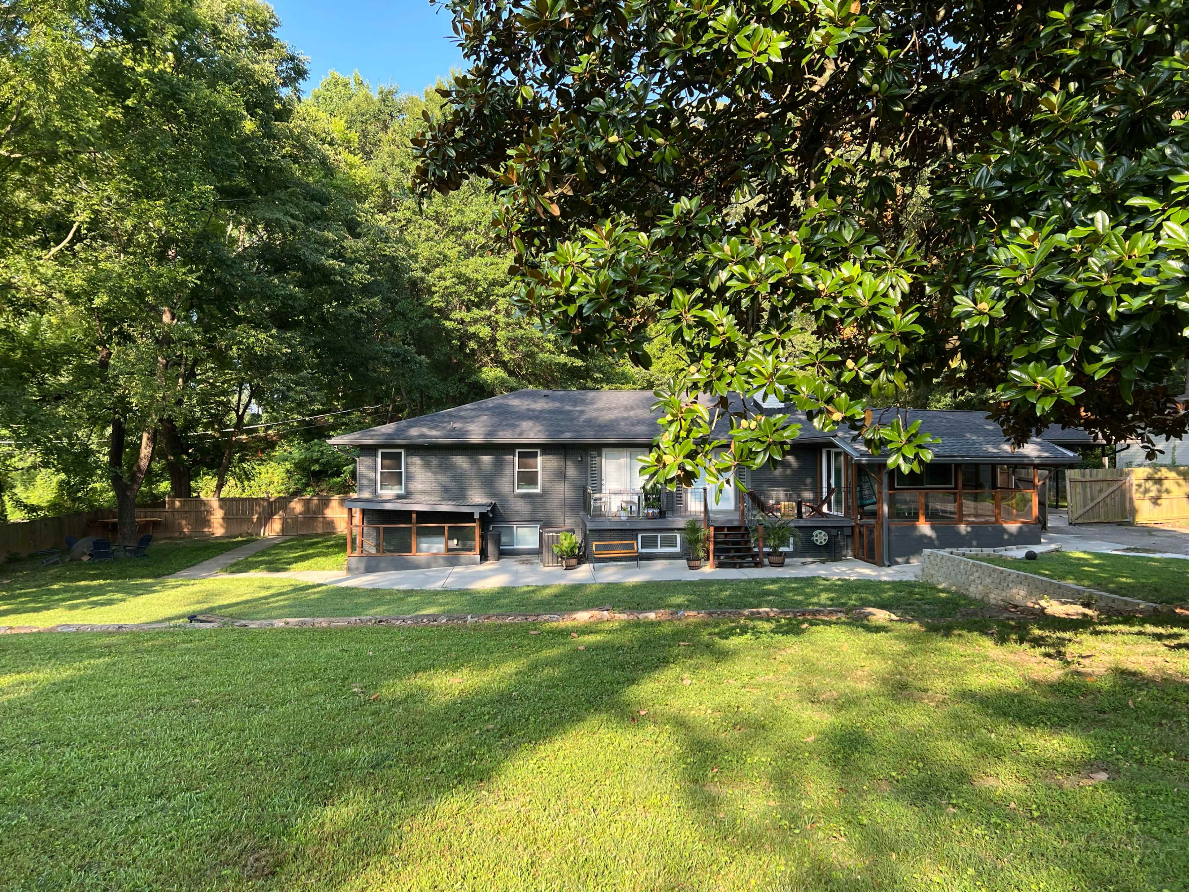 A single-story house with a dark exterior is set against a backdrop of trees and a grassy yard.