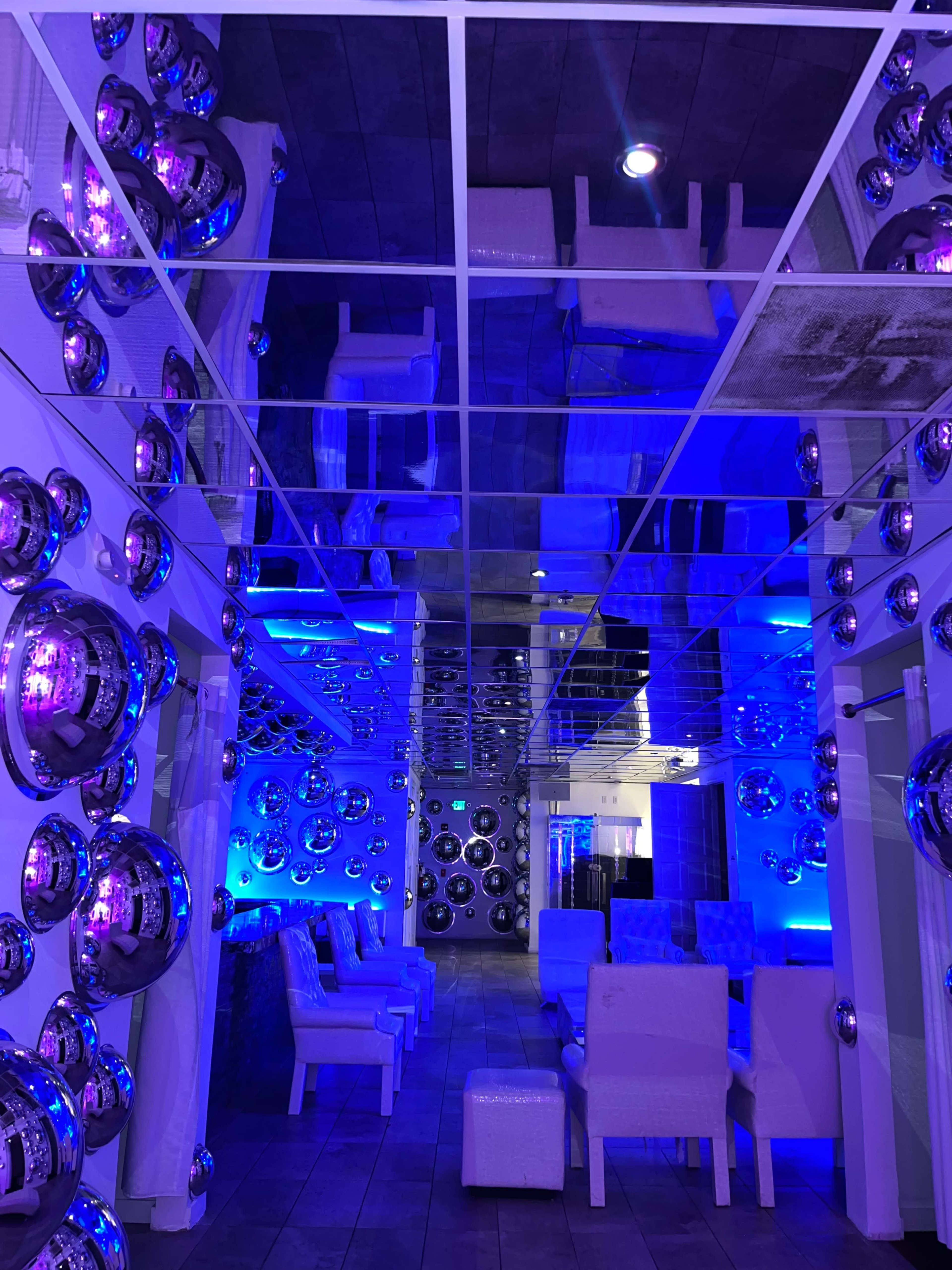 The image shows a modern interior space with a mirrored ceiling, illuminated by blue lighting and decorated with spherical metallic objects on the walls.