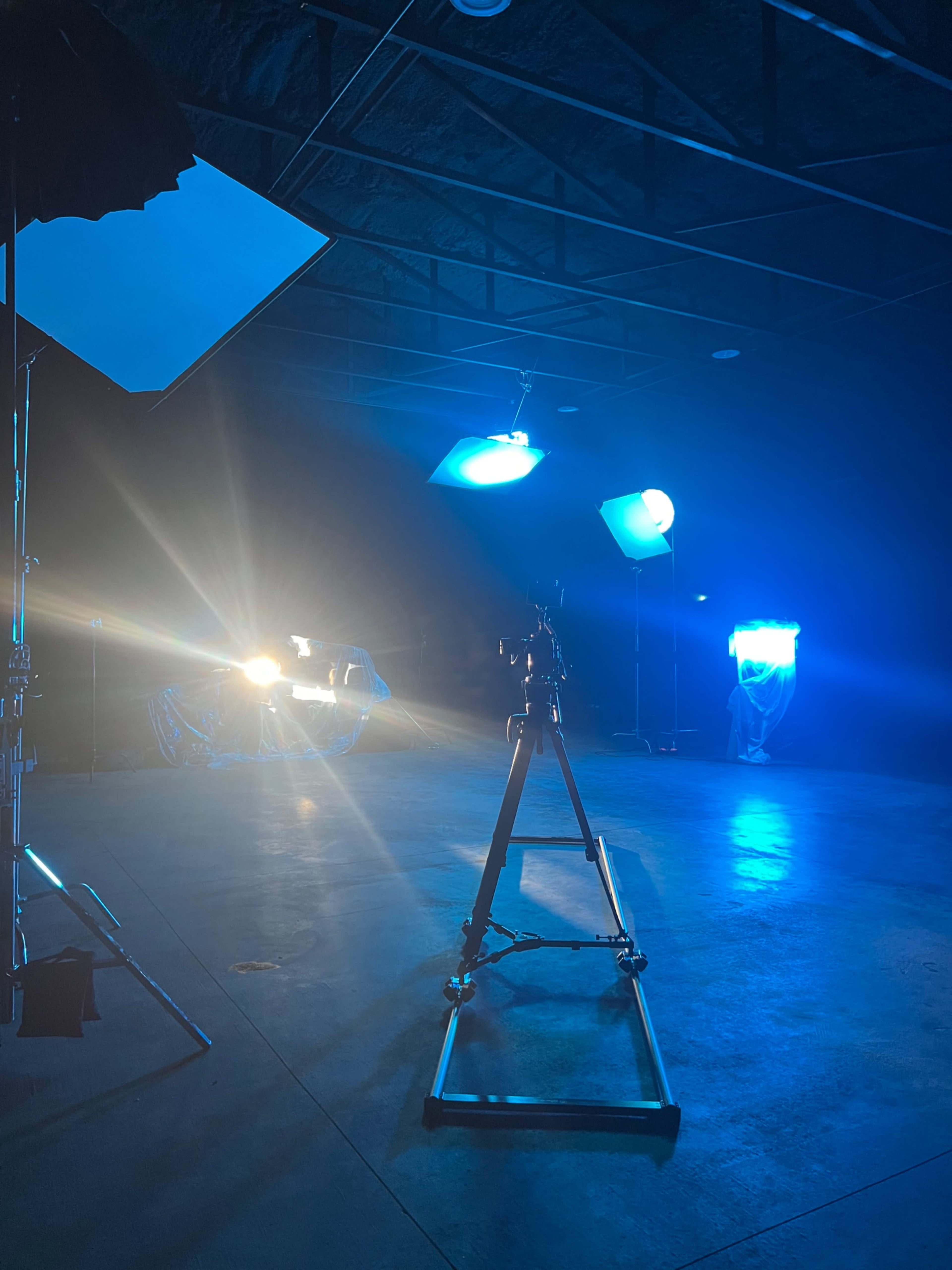 A dimly lit studio space equipped with multiple lighting setups and a camera on a tripod.