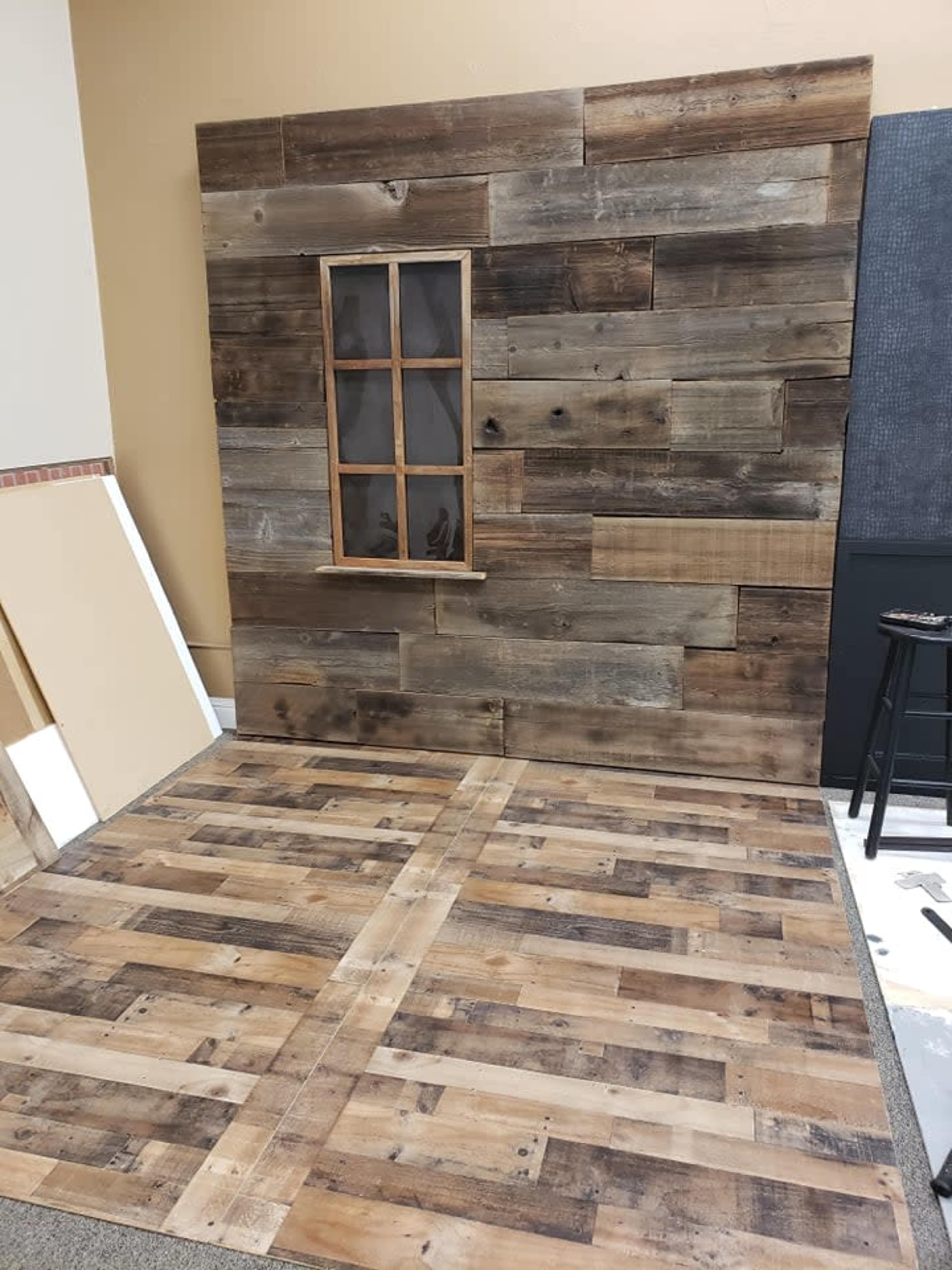 A wooden wall with a window frame and a wooden floor, both featuring a rustic design.
