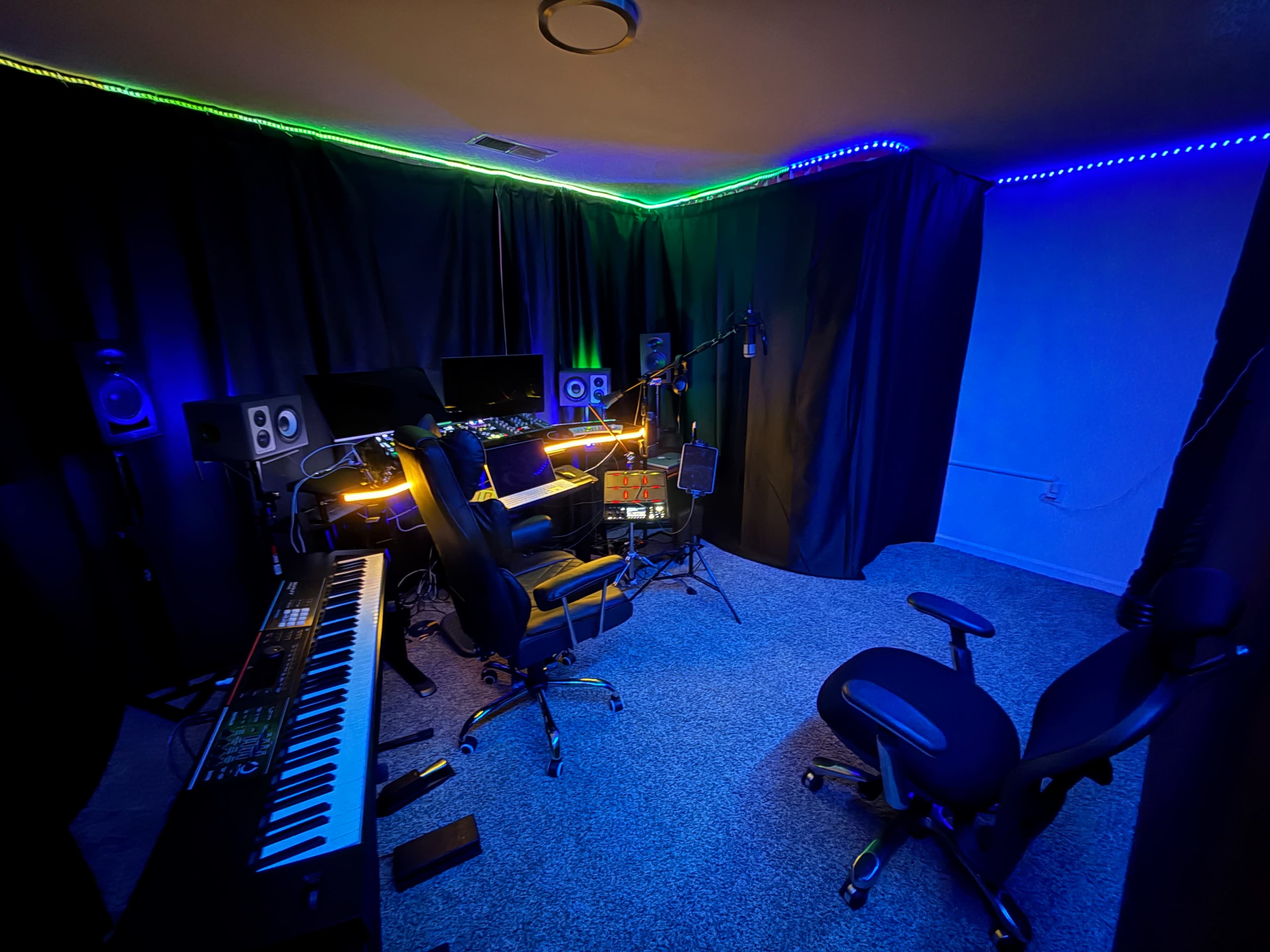 The image shows a dimly lit music studio with a keyboard, two office chairs, and various audio equipment, highlighted by colorful LED lighting along the ceiling.