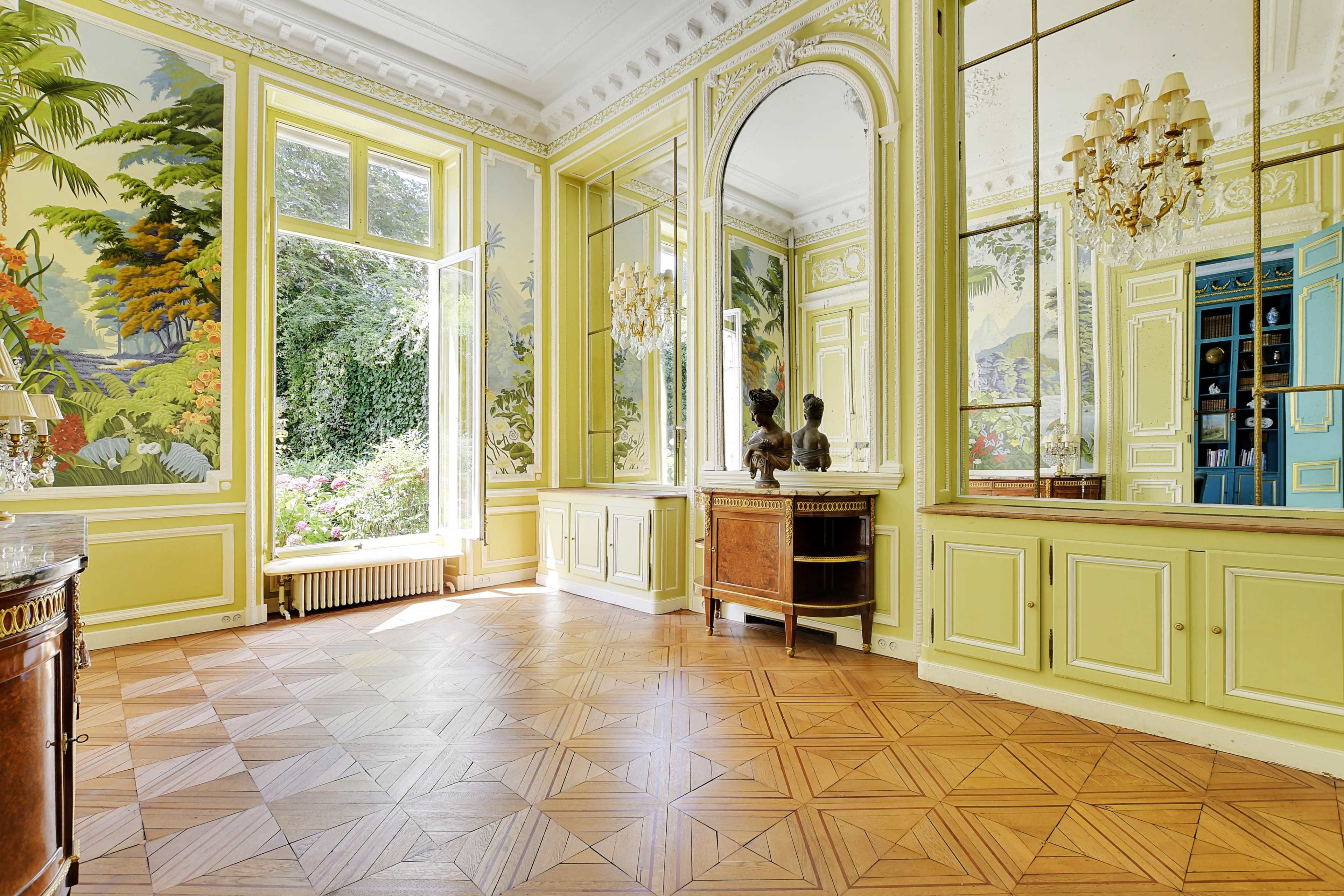 The room features yellow walls adorned with large mirrors and tropical murals, with wooden flooring and a decorative cabinet along one side.