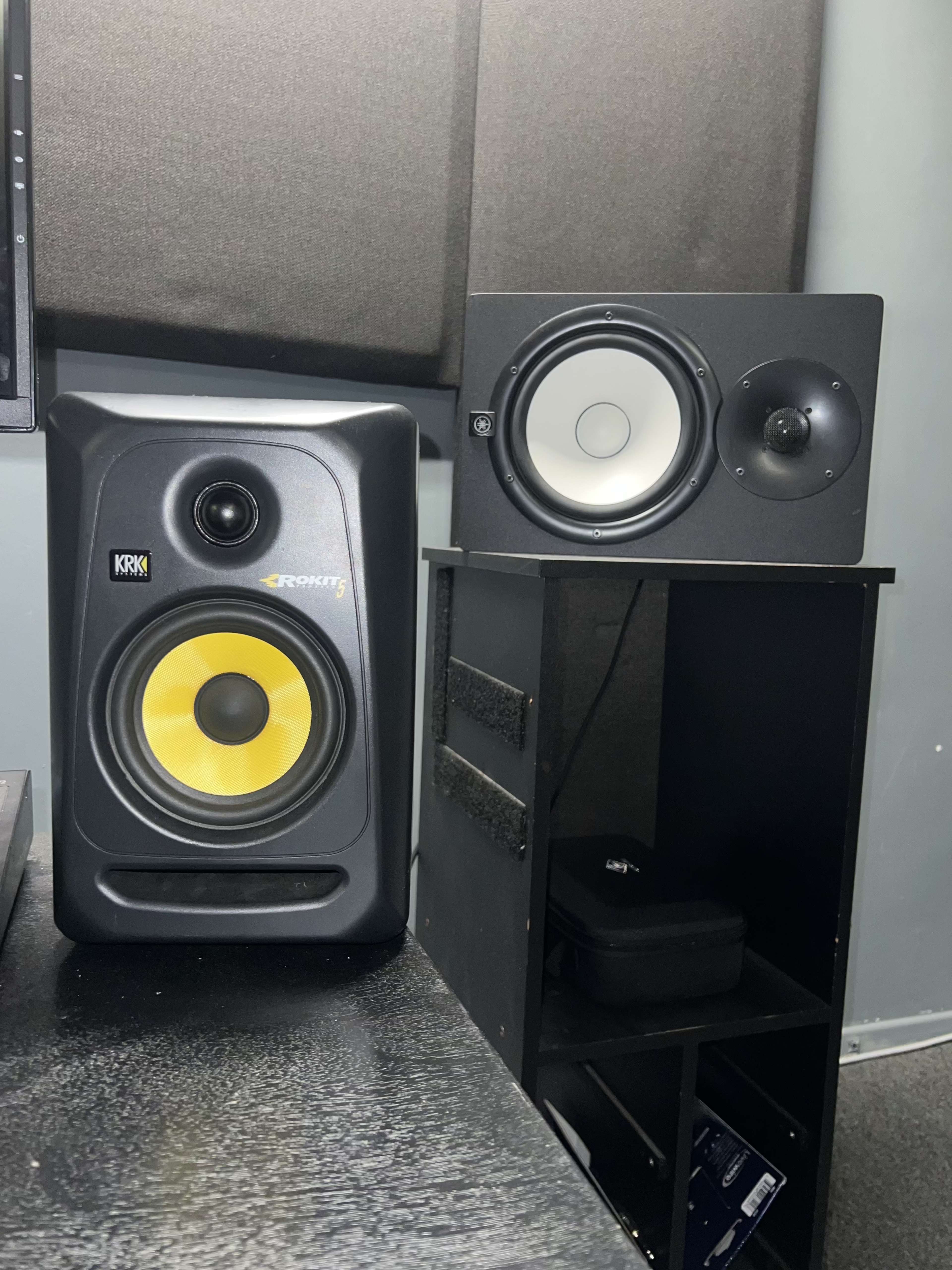 A pair of studio monitors on a black table with a soundproof backdrop.