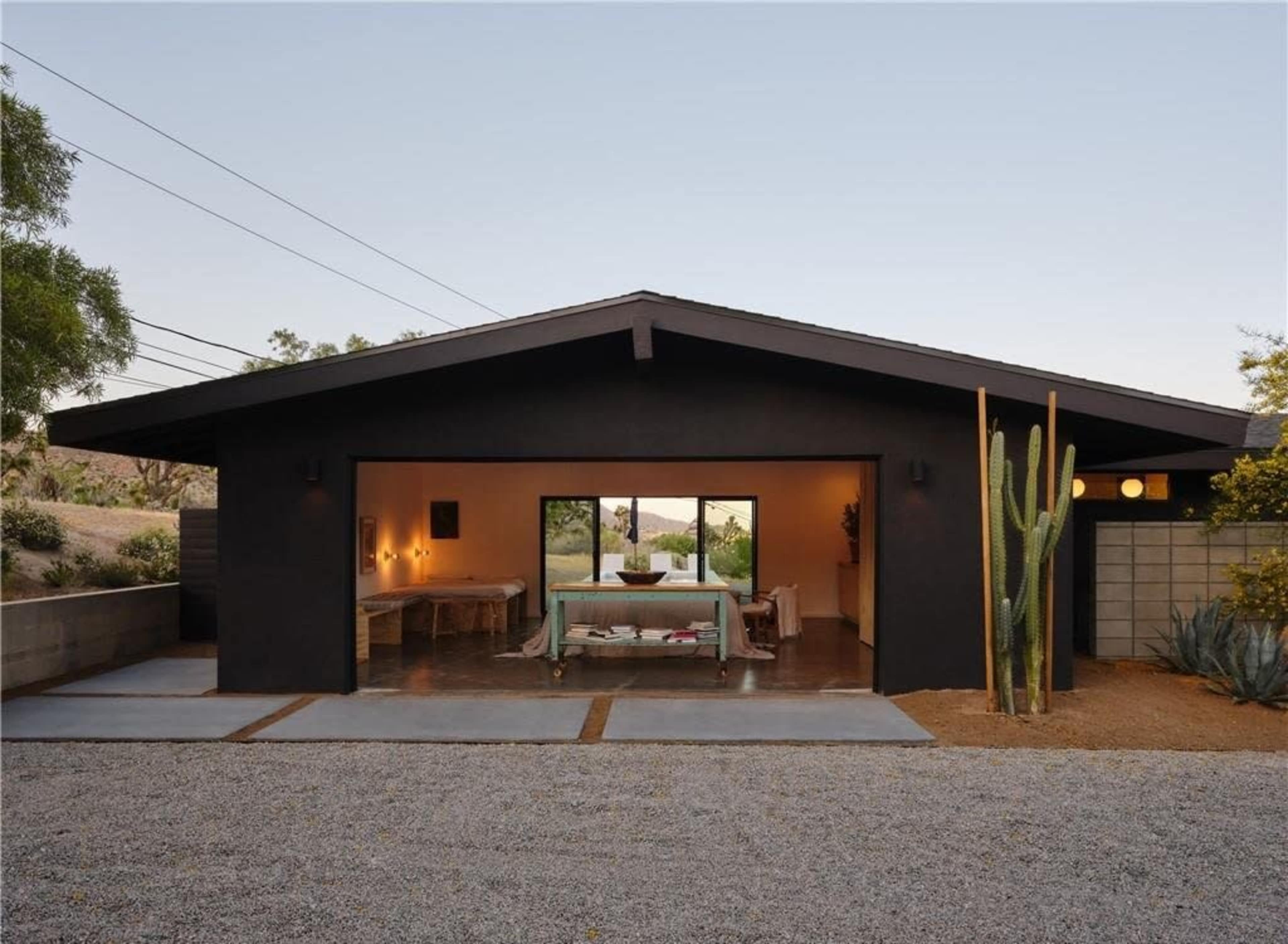 A modern black house with a large front window and minimalist landscaping features cactus and gravel paths.