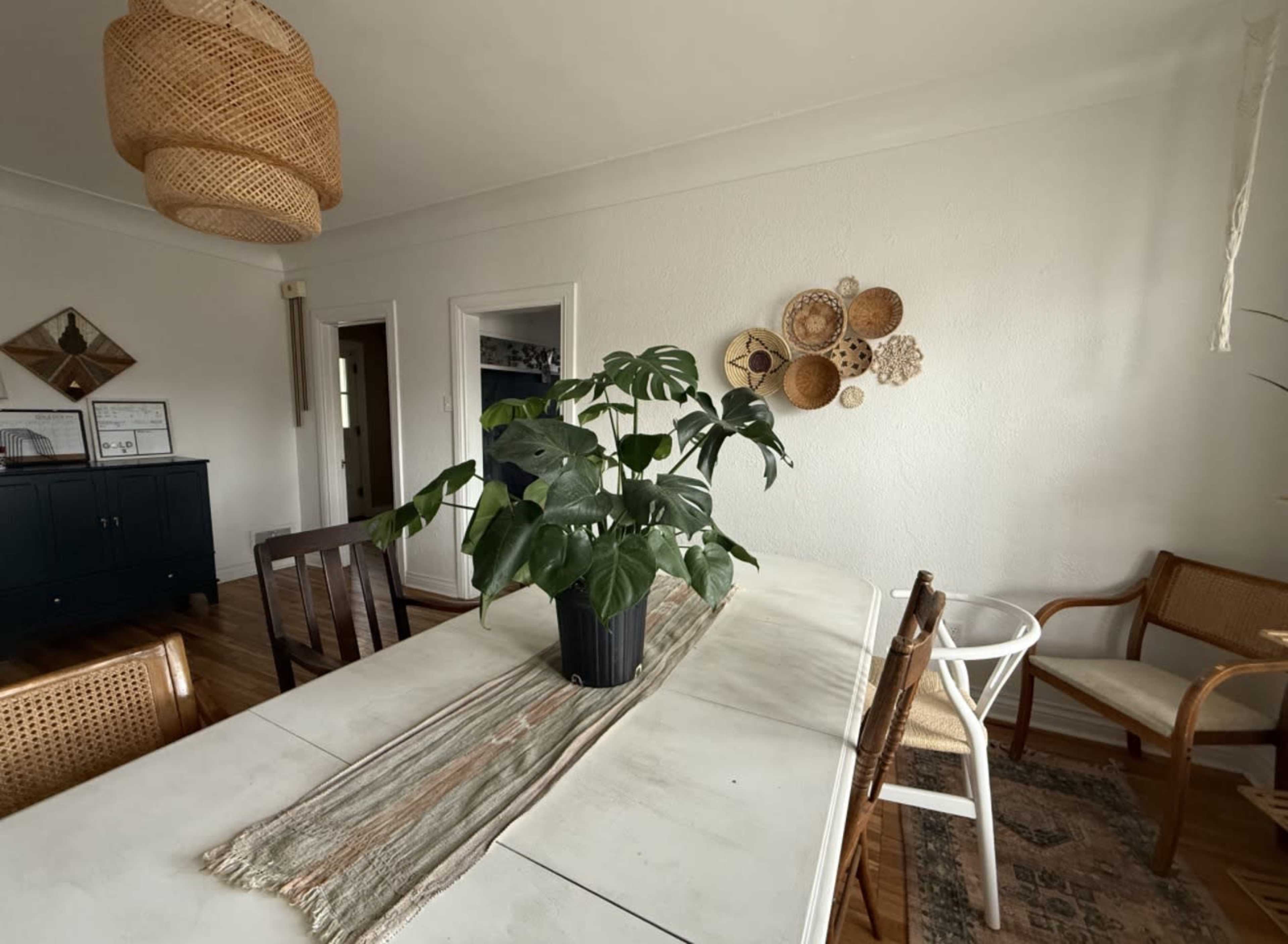 A dining area features a table with a plant centerpiece, surrounded by various chairs and decorated with wall hangings.