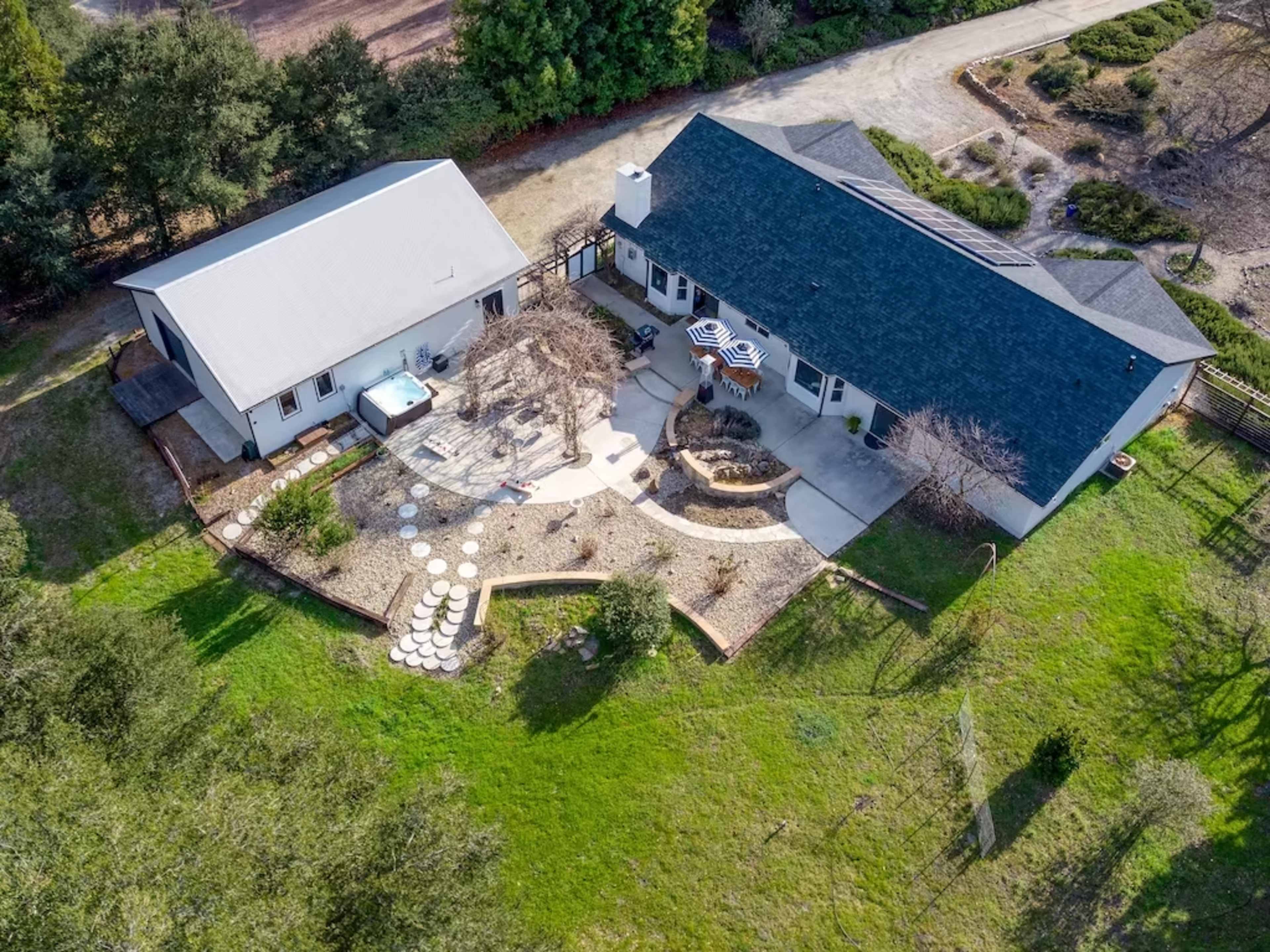 A large property featuring two buildings, a patio area with outdoor seating, and landscaped gardens.