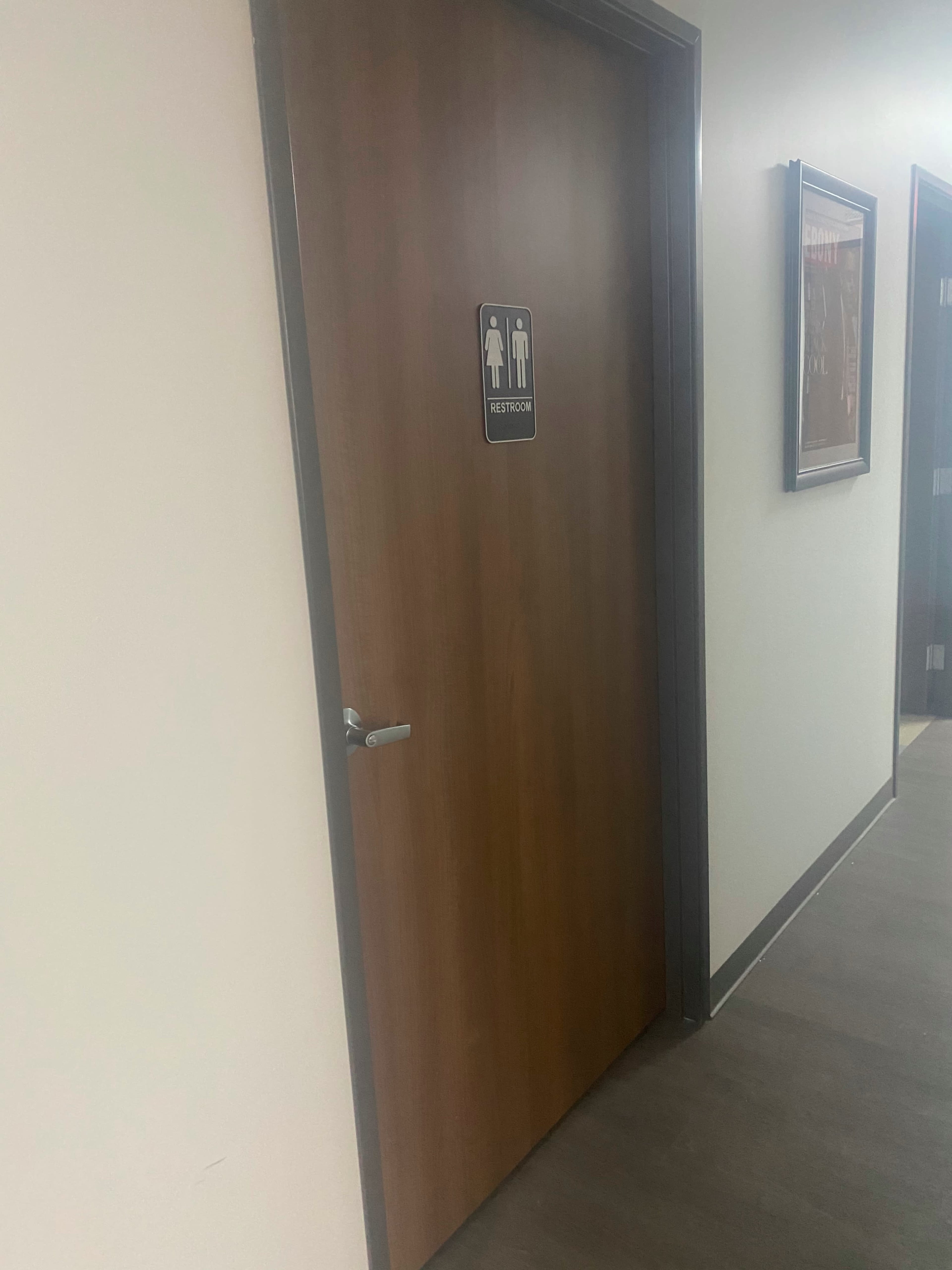 A wooden restroom door with a sign indicating men's and women's facilities is shown in a hallway.
