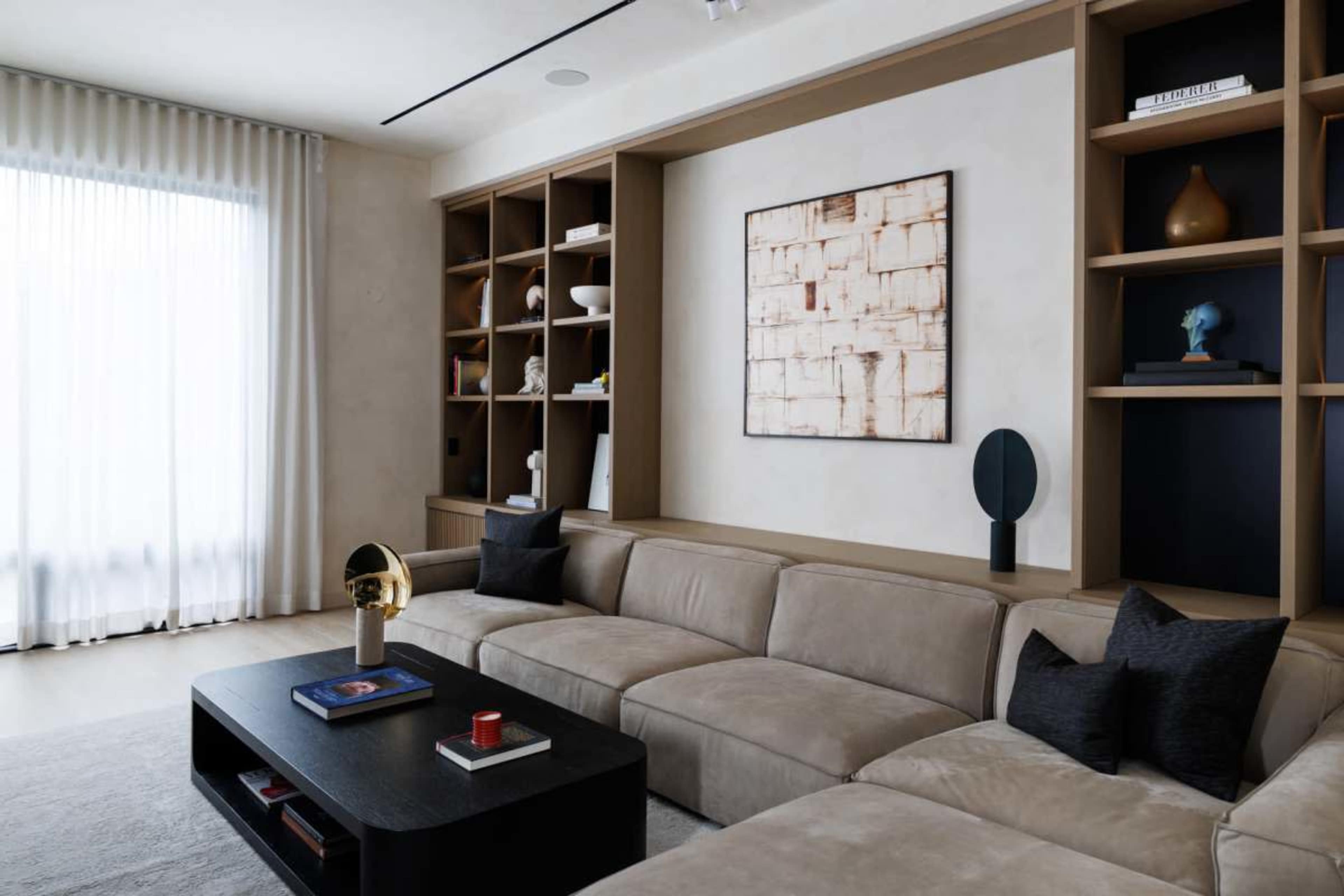 The image shows a modern living room with a sectional sofa, a coffee table, and built-in shelves displaying decorative items and art.