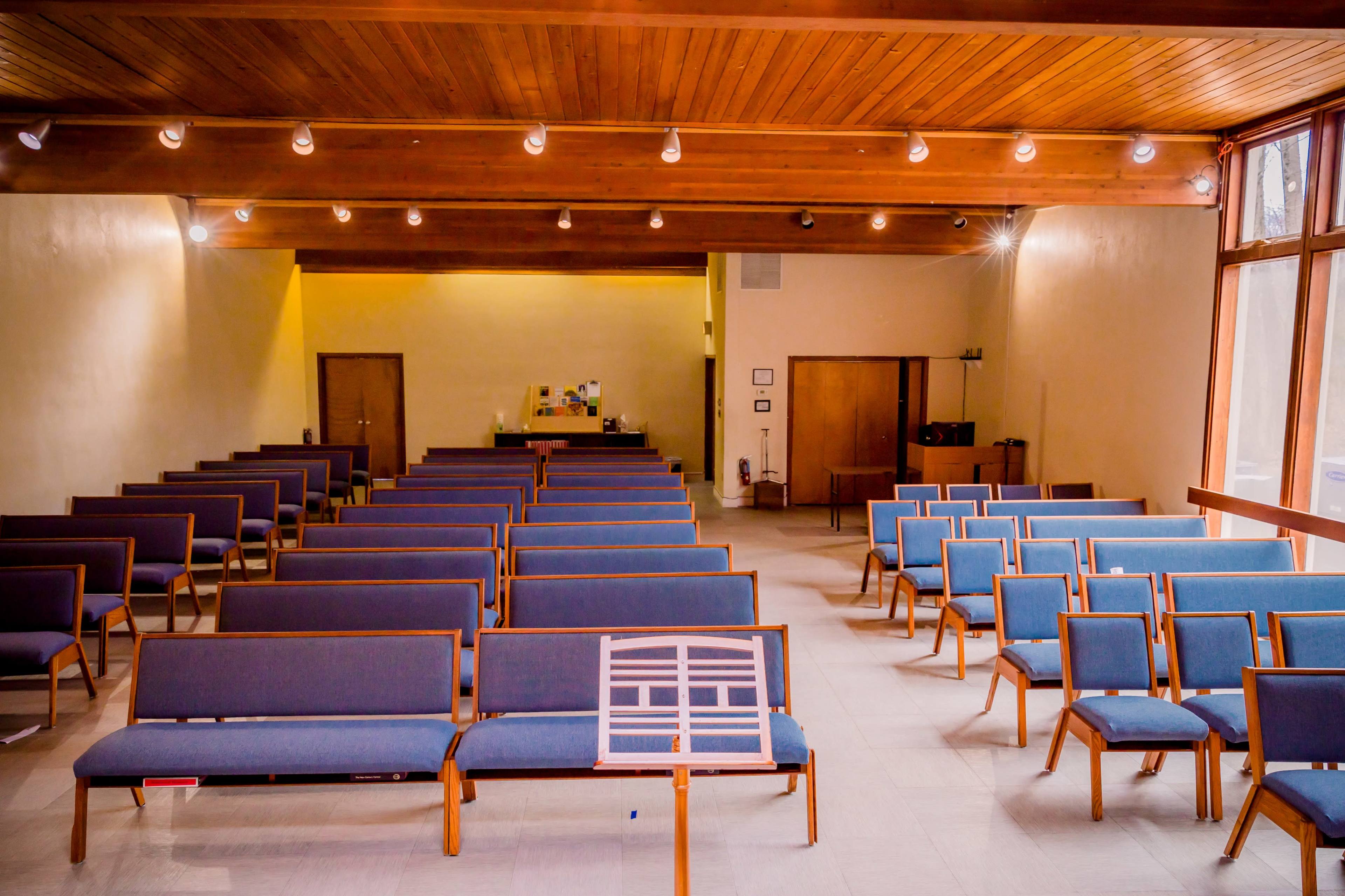A spacious, empty auditorium with rows of blue chairs facing a small stage area at the front.