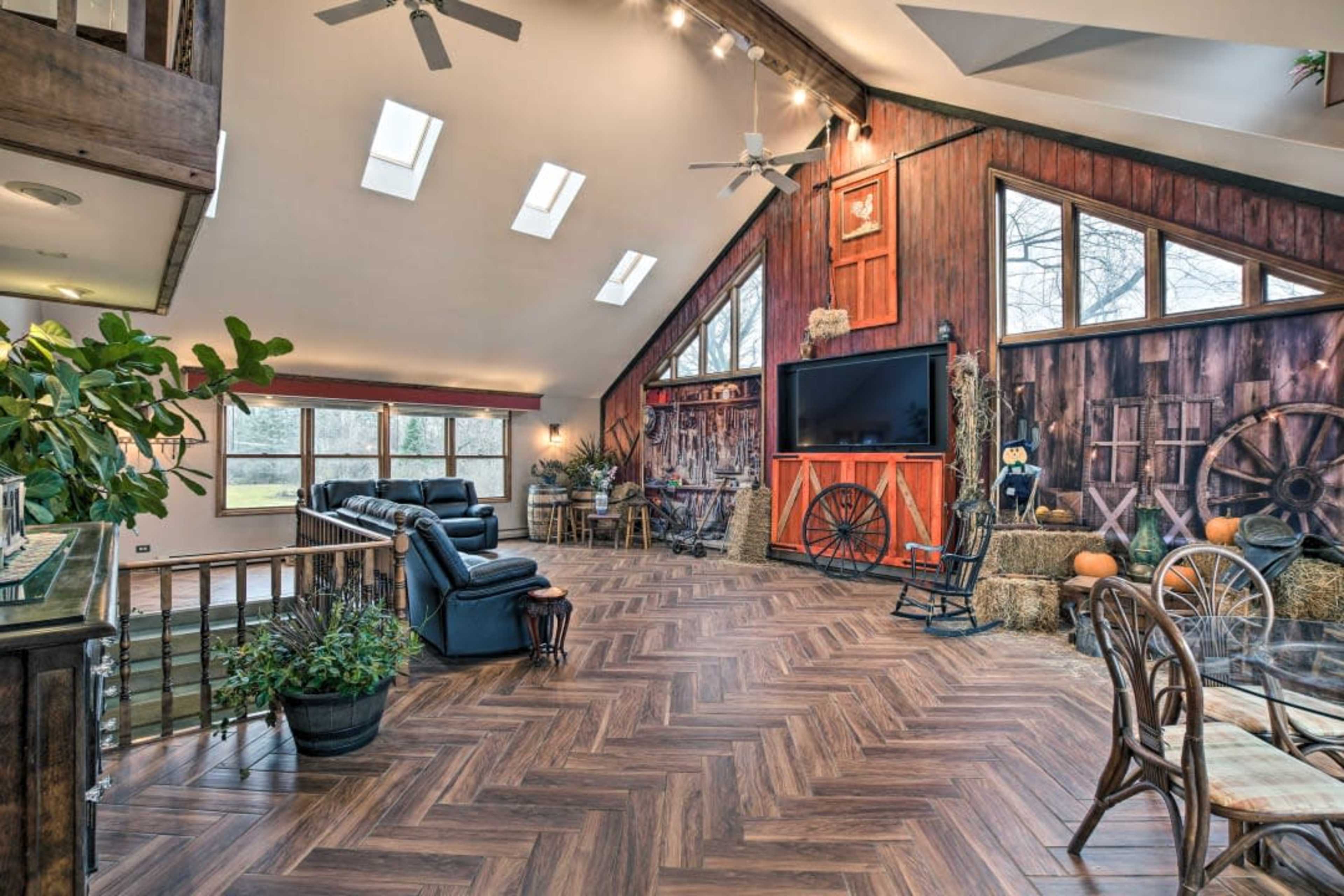 The interior of a spacious living area features wooden accents, a large television, and a mix of rustic decor, including a rocking chair and hay bales.