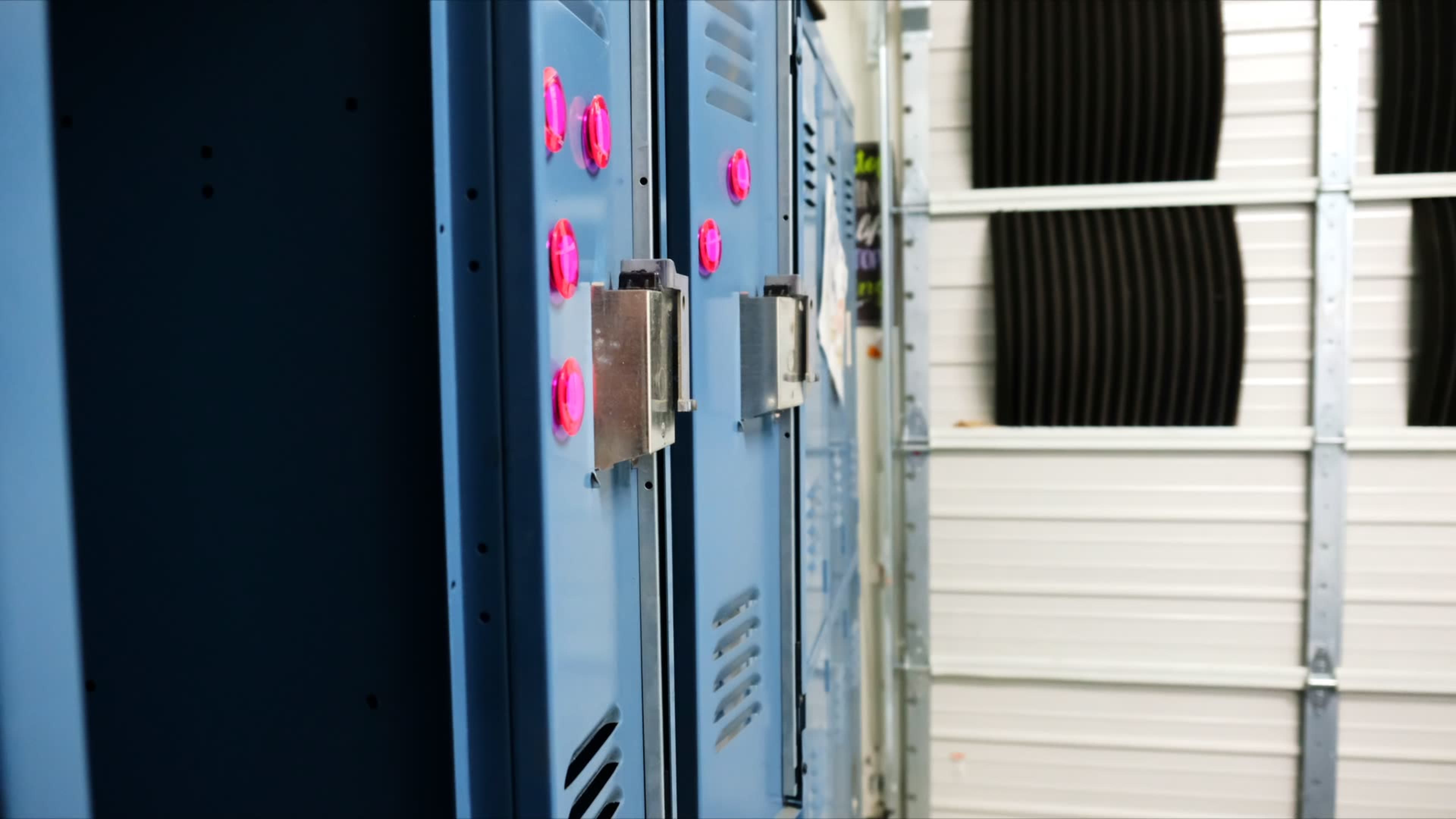 The image shows a row of blue lockers with pink combination dials in a storage area.