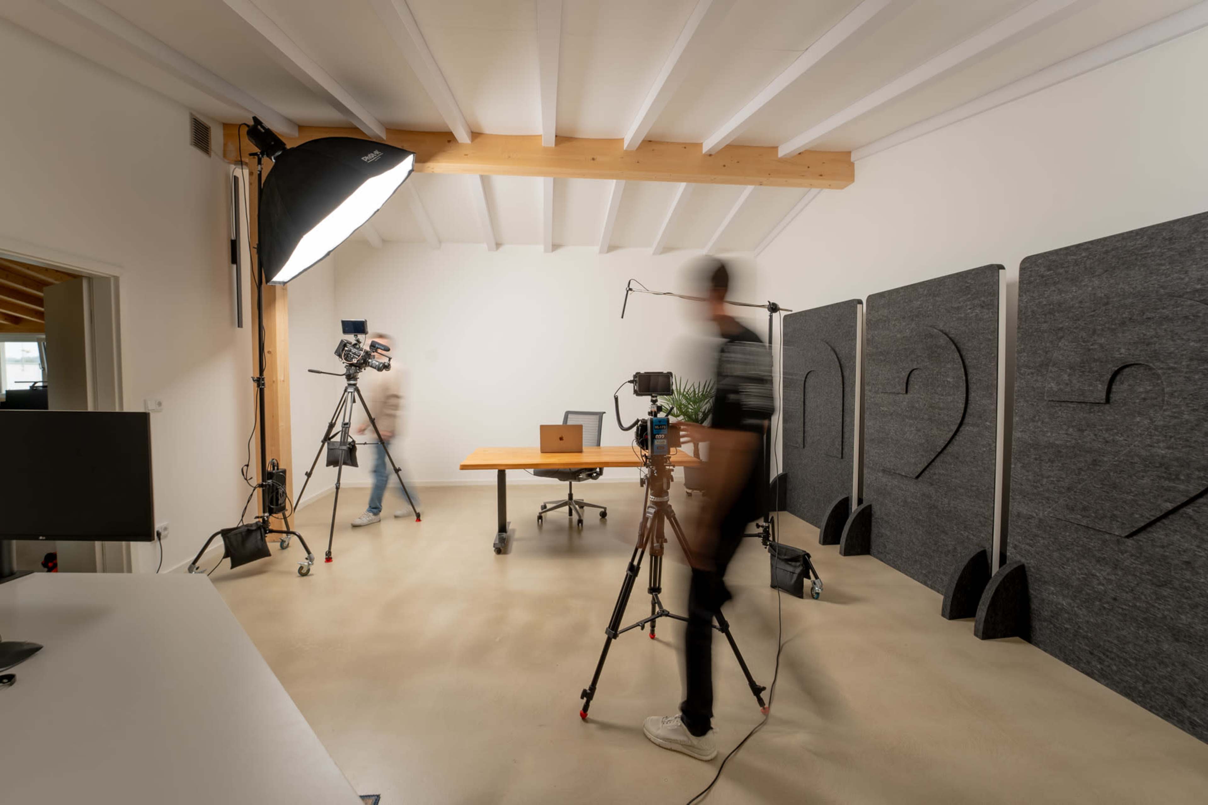 A camera crew sets up equipment in a minimalistic studio with a central table and soft lighting.