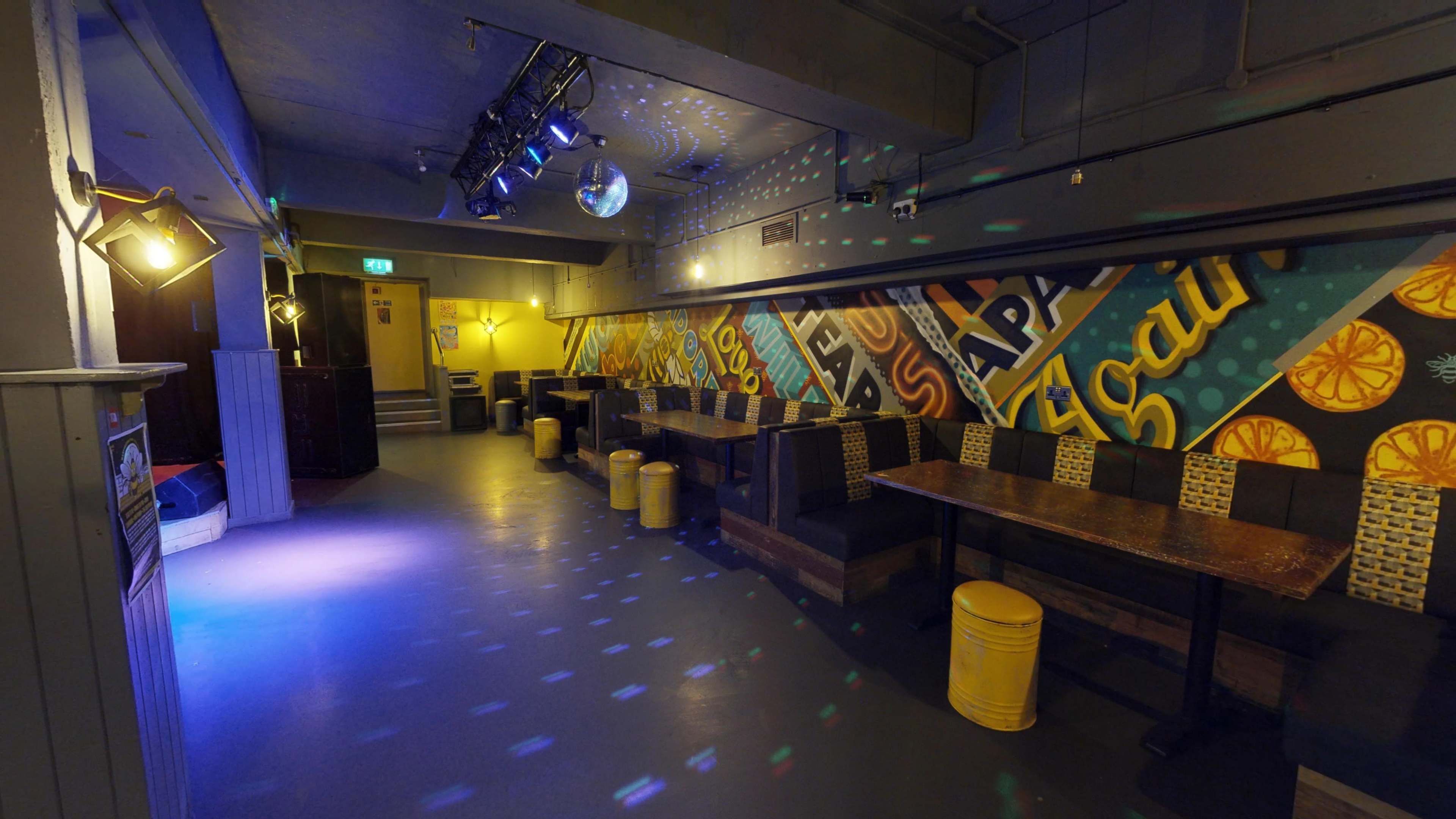 The image shows an empty bar area with colorful graffiti-style wall art, a disco ball hanging from the ceiling, and seating along the walls.